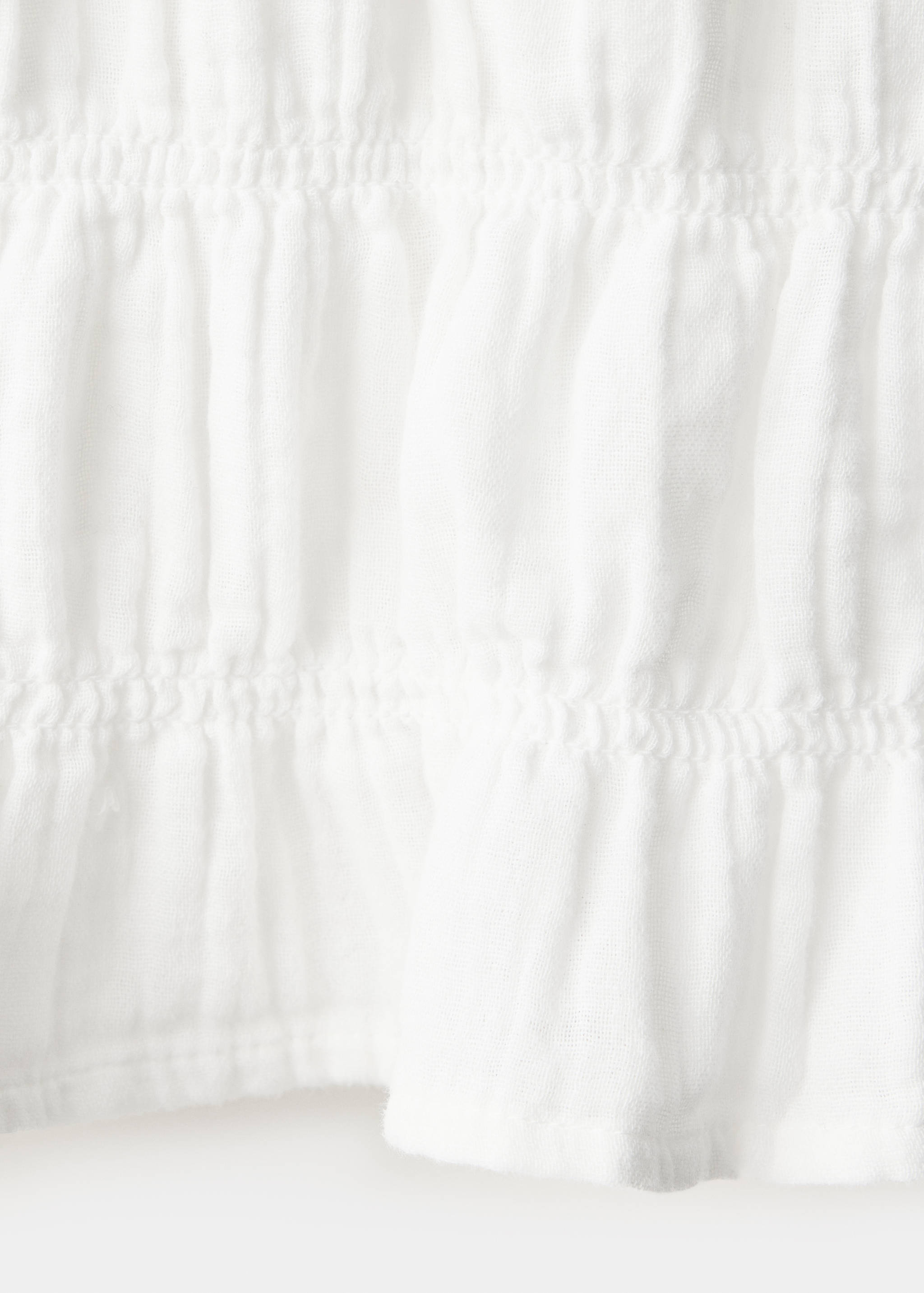 Close-up of white textured shirt fabric with smocked ruffles.