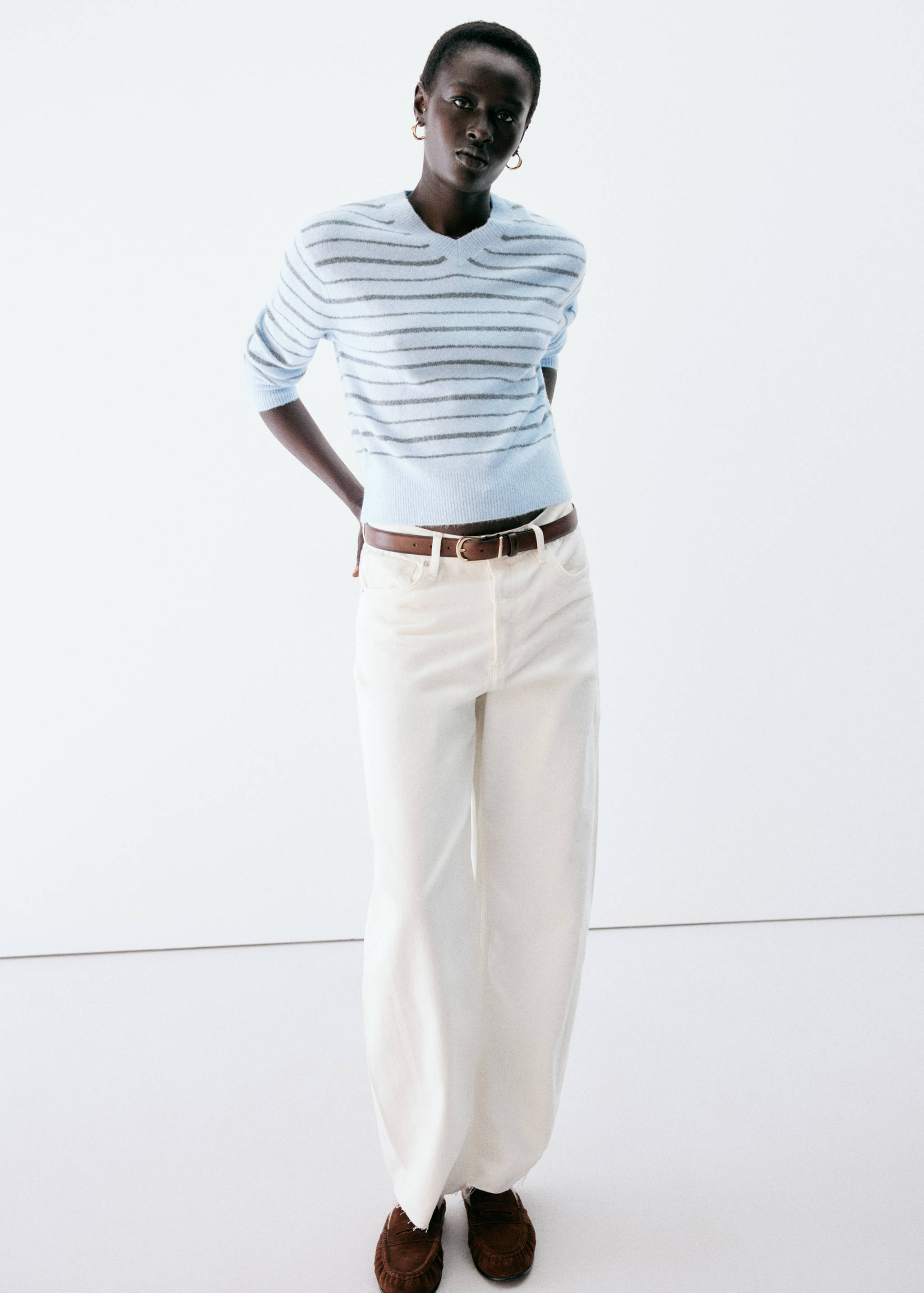 Jersey de cuello en V de rayas en azul claro y gris, combinado con pantalones blancos.