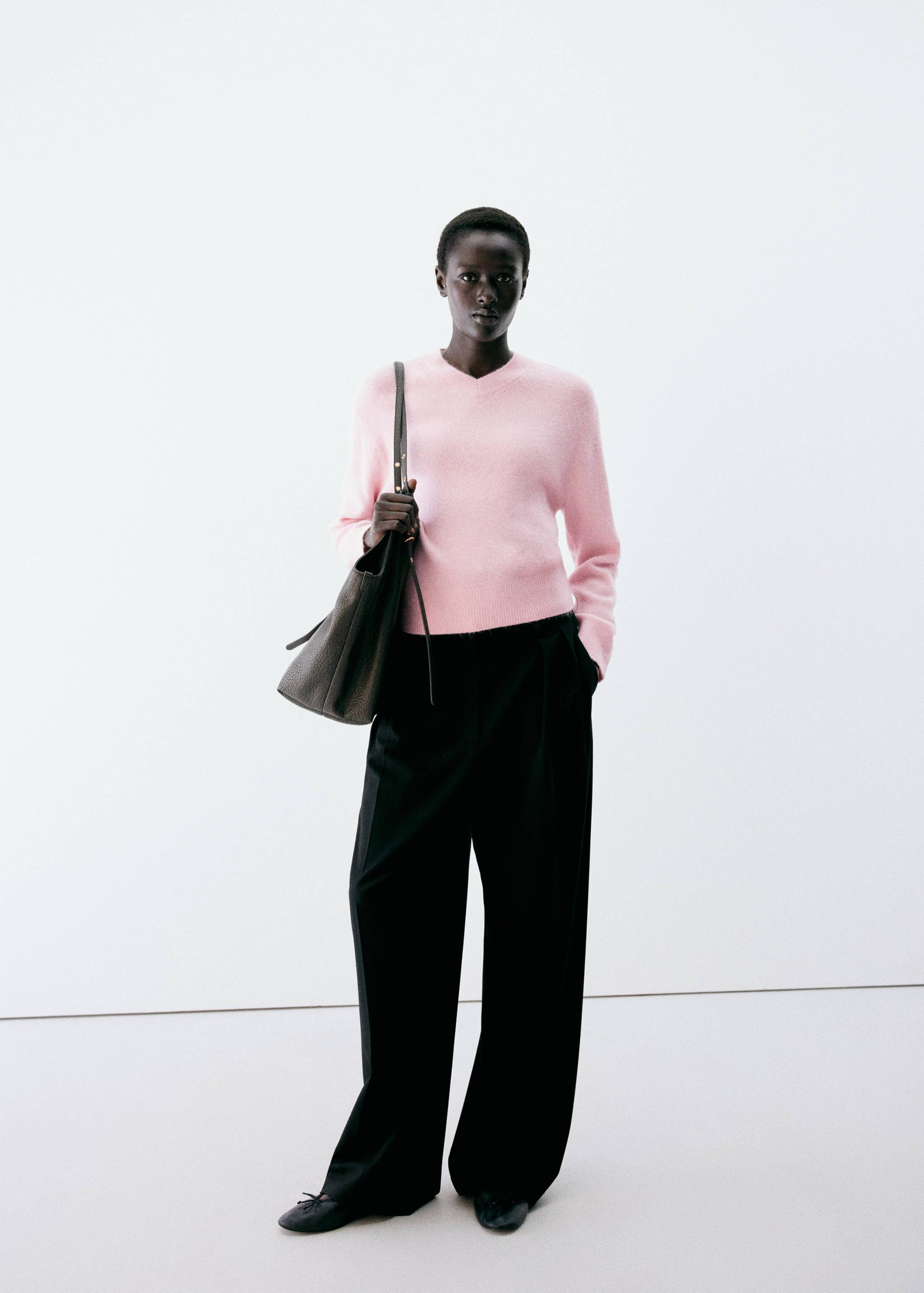 Pink V-neck jersey with long sleeves worn with black trousers and a dark brown shoulder bag.