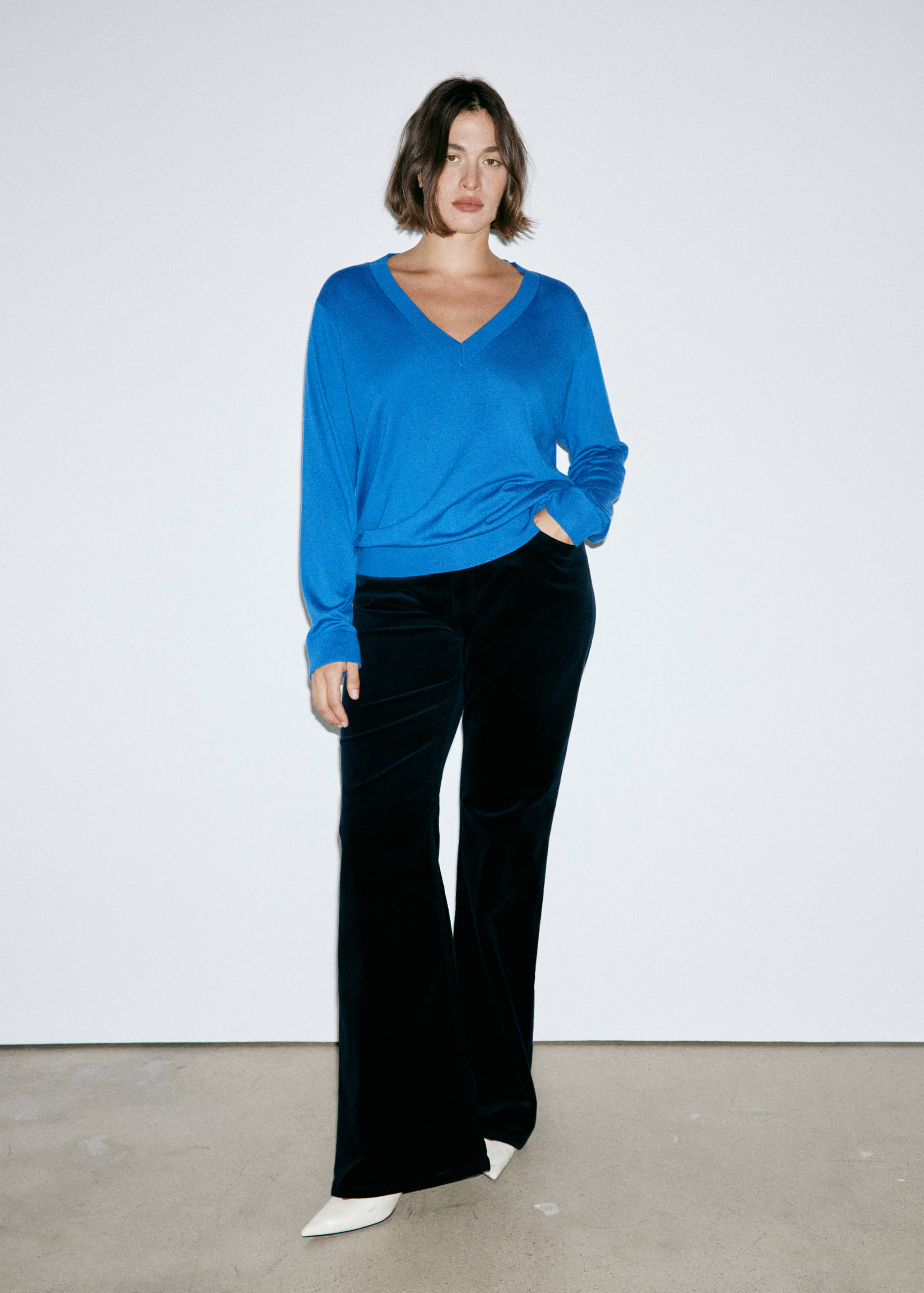 Blue V-neck jumper worn with dark flared trousers.