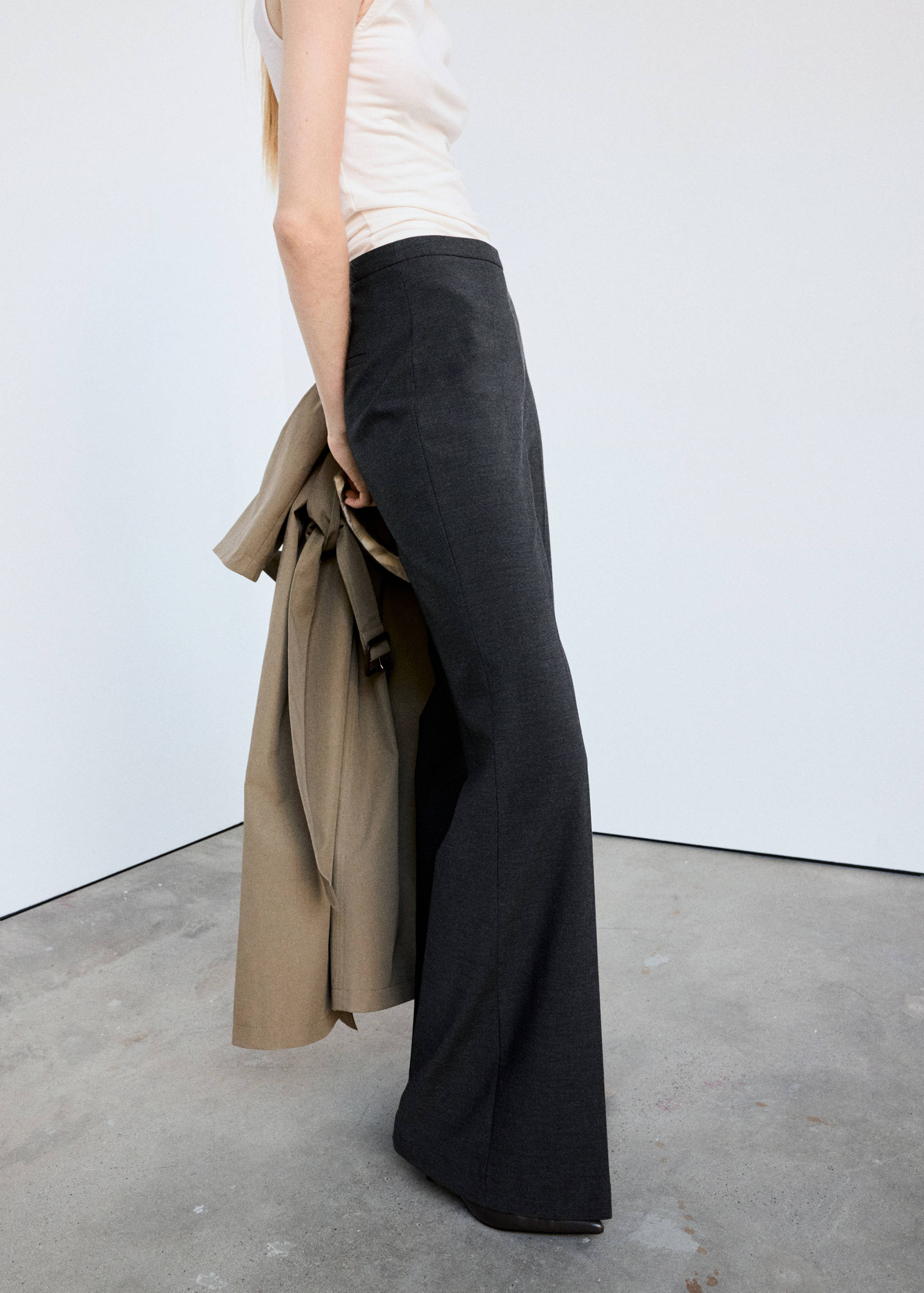 Dark grey high-waisted flared trousers worn with a light top and a trench coat.