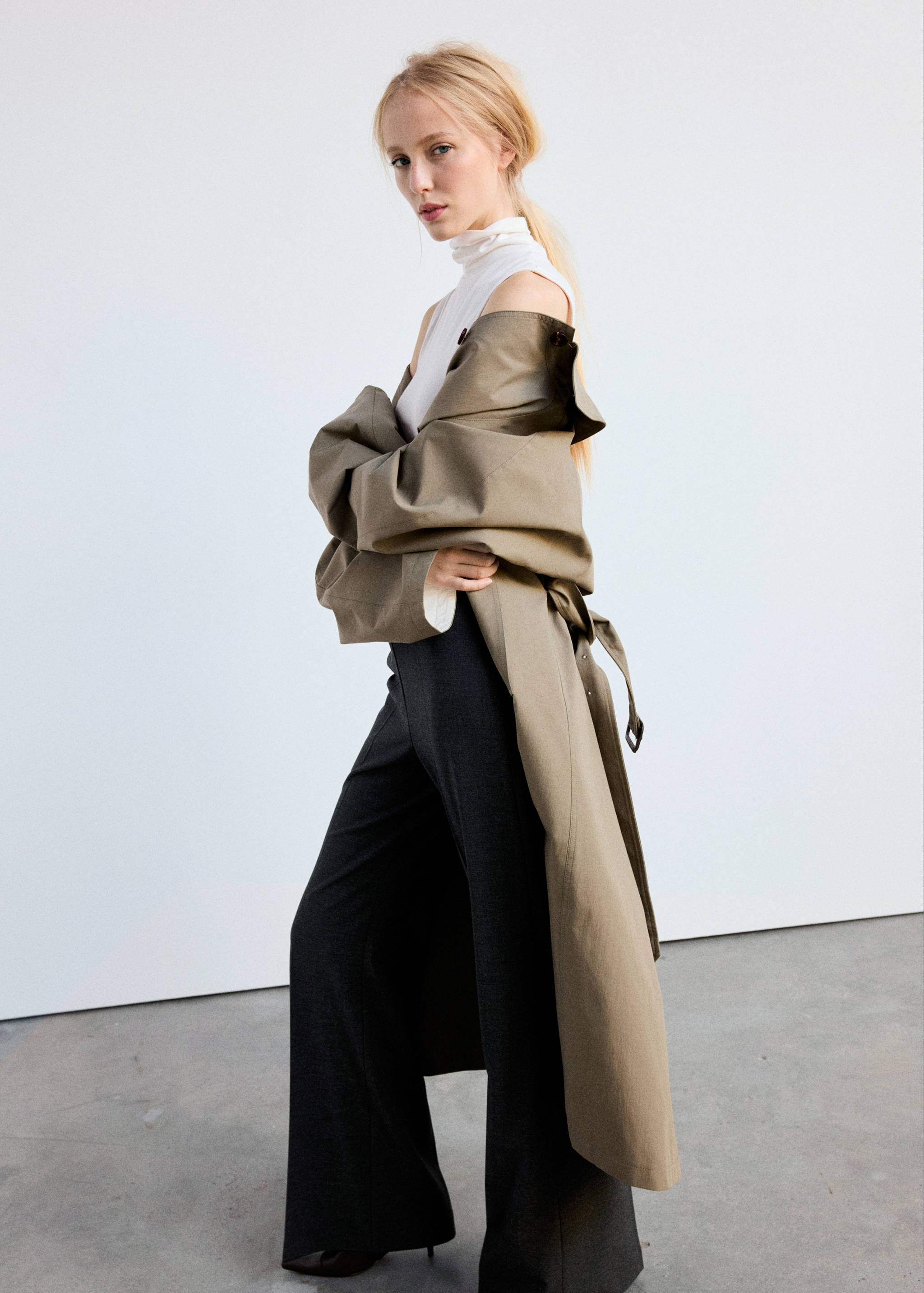 Dark grey trousers worn with a white top and oversized khaki trench coat.