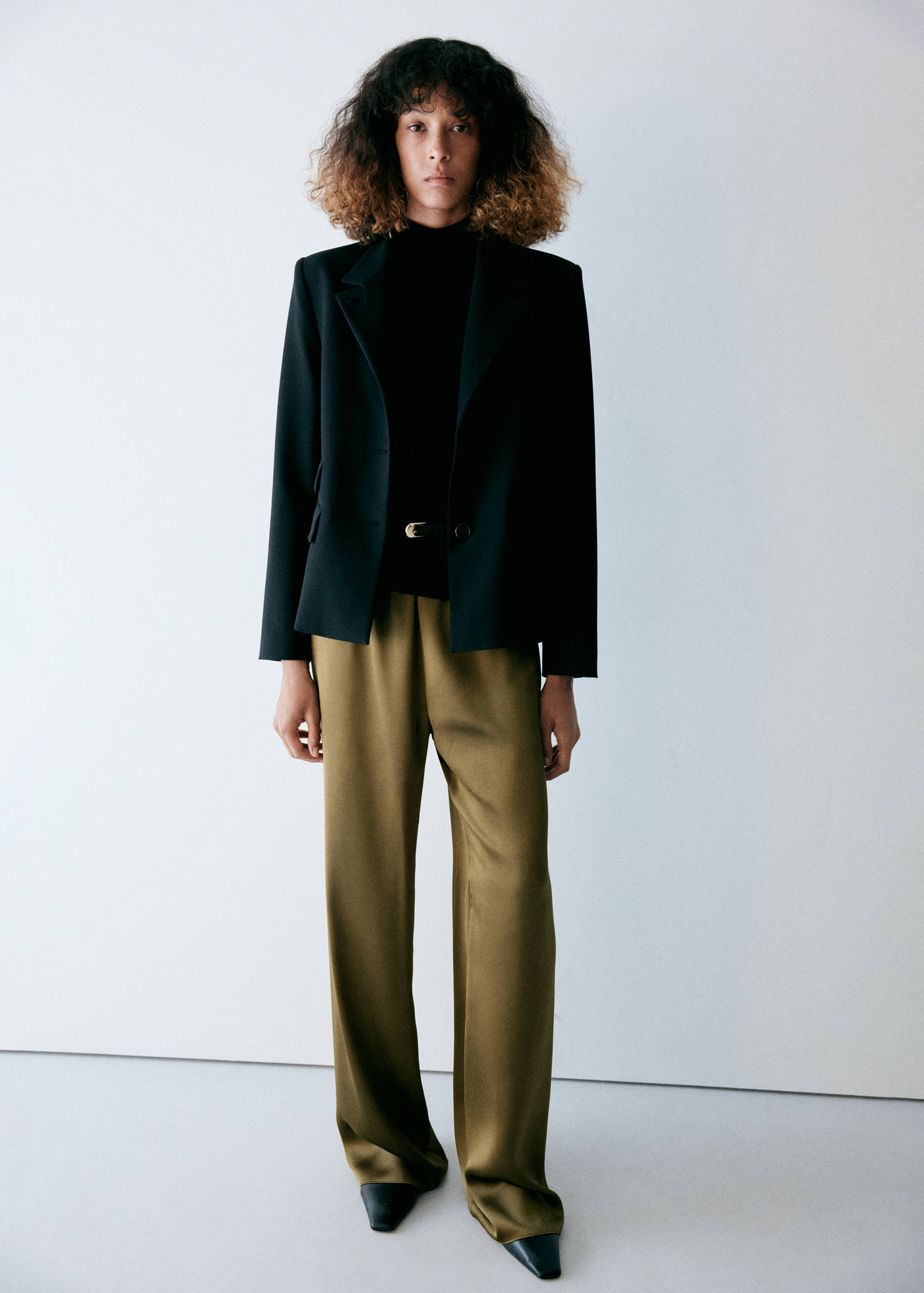 Olive green relaxed-fit trousers worn with a black top and blazer.