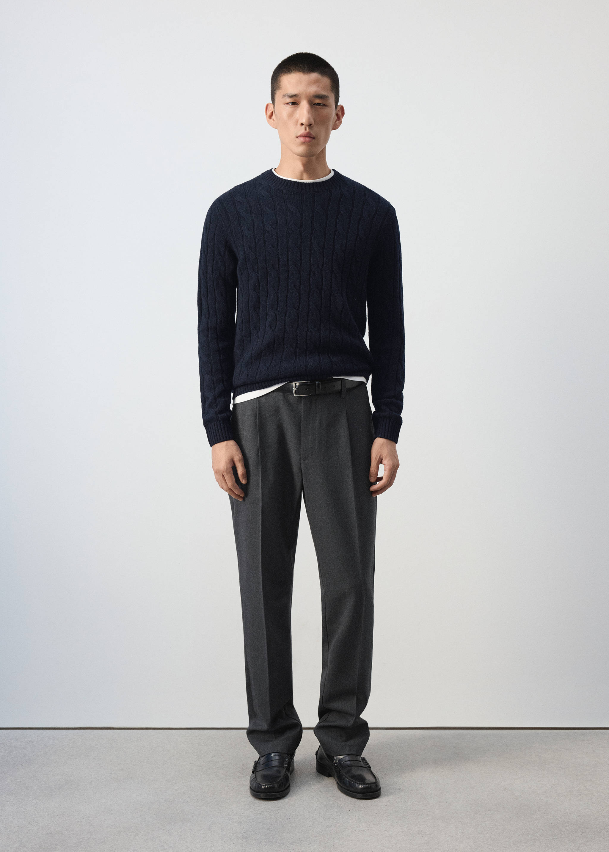 Navy blue cable-knit crew-neck jersey worn with dark grey trousers.