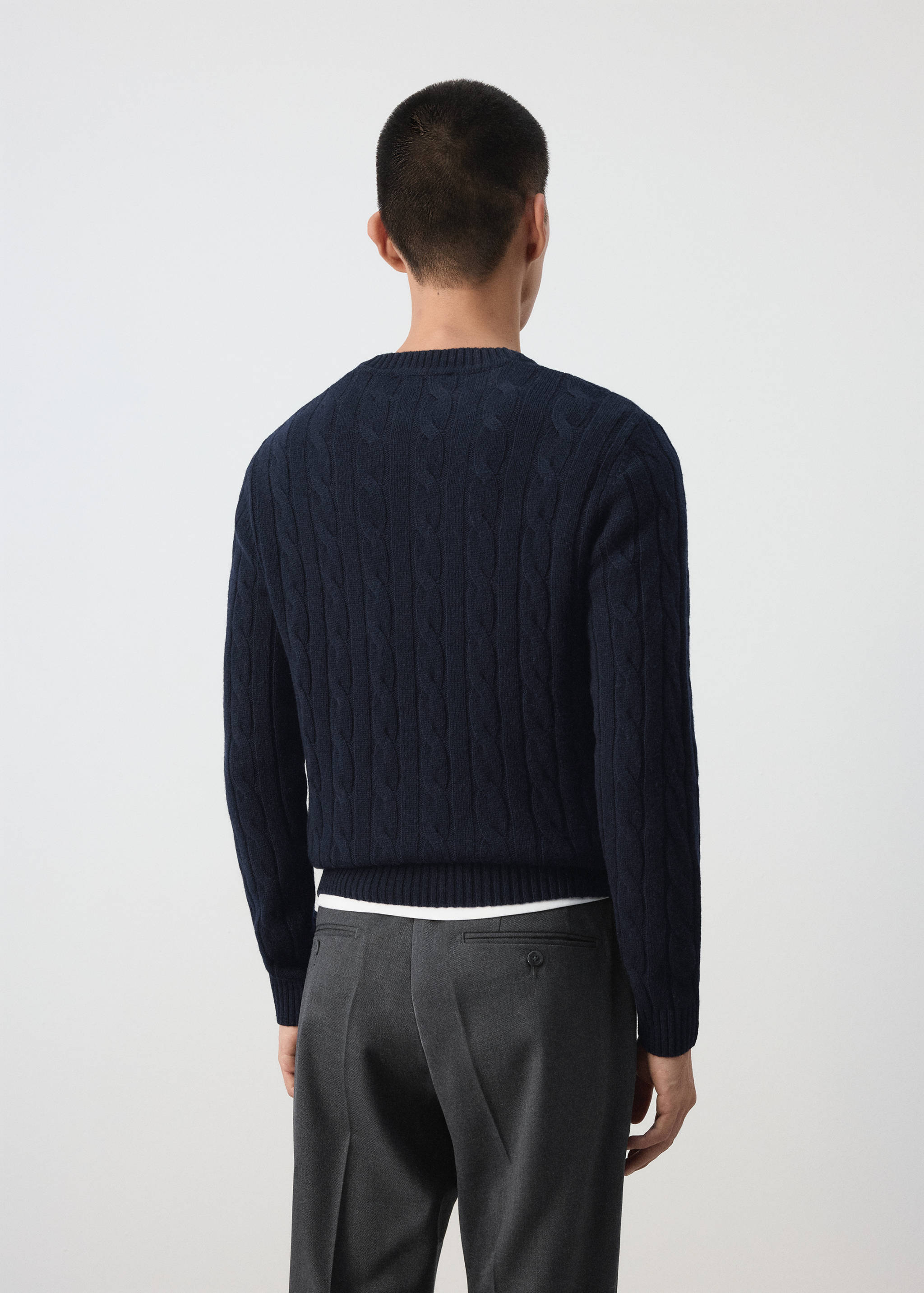 Navy blue cable-knit jumper seen from the back on a model.