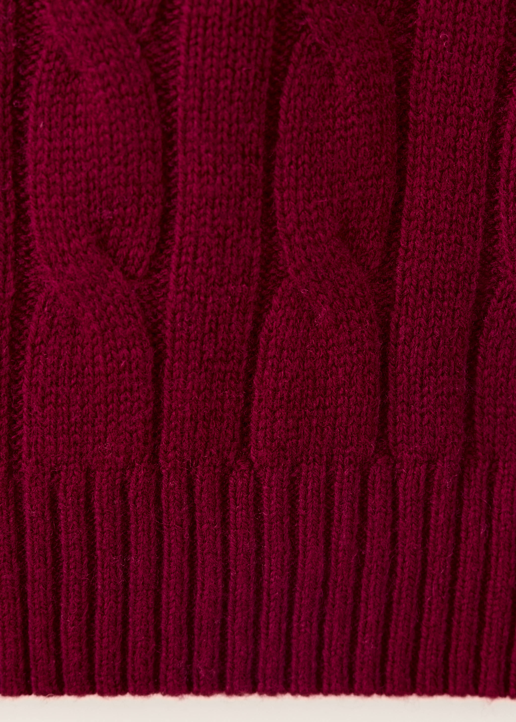 Burgundy cable-knit jumper fabric detail showing ribbed hem.