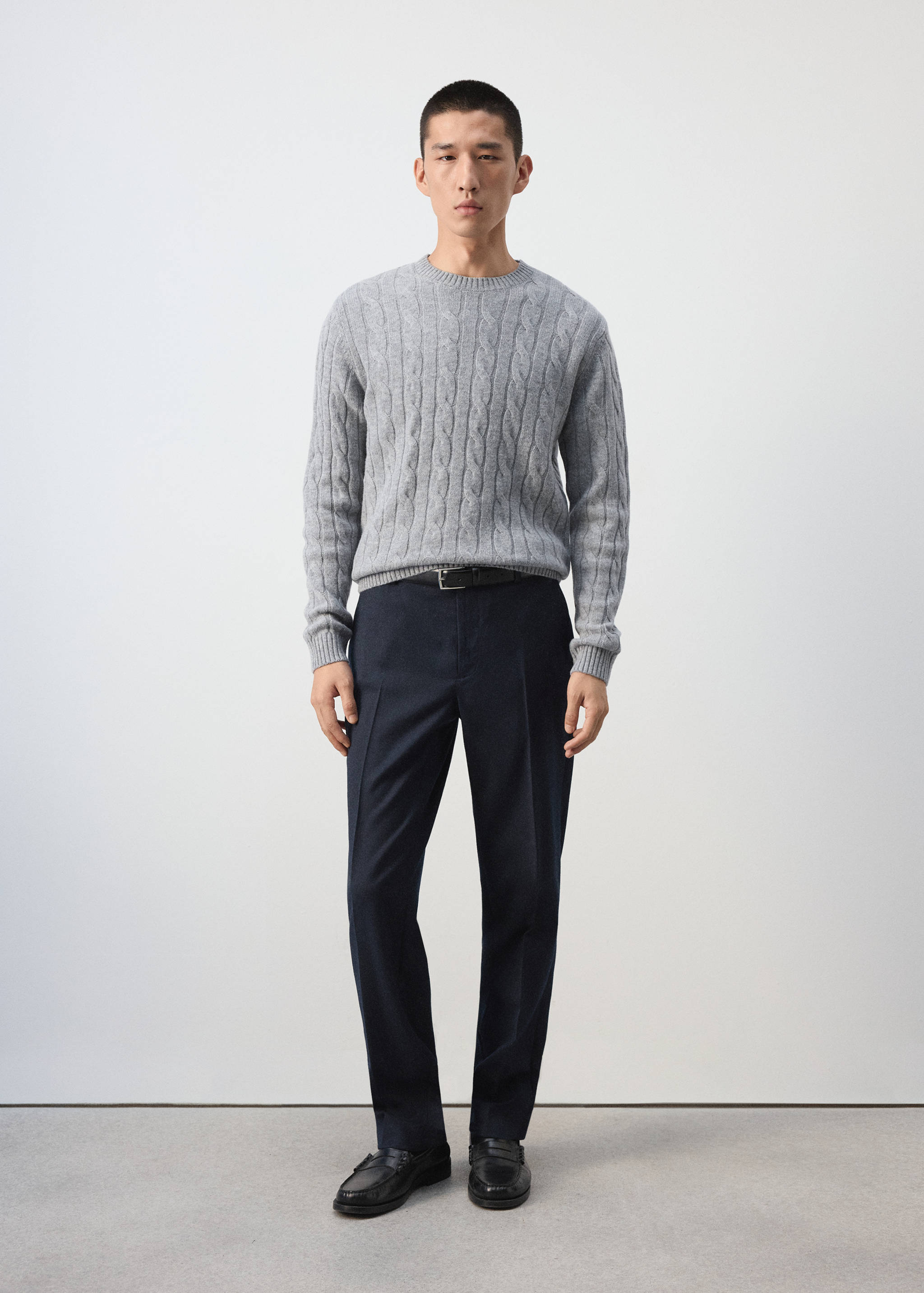 Grey cable-knit crew-neck jersey sweater worn with dark trousers.