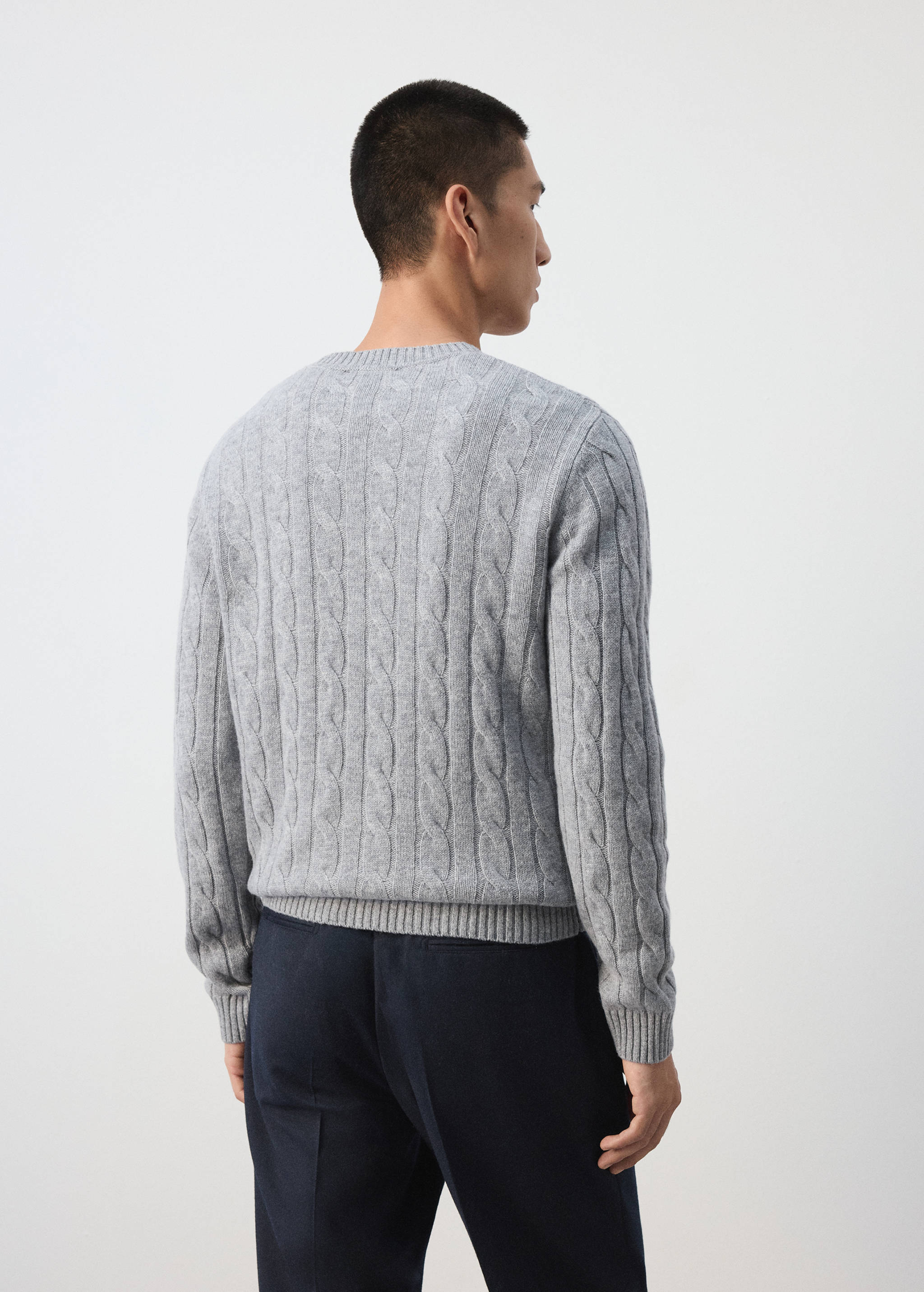 Back view of a light grey cable-knit sweater with a ribbed crew neck.