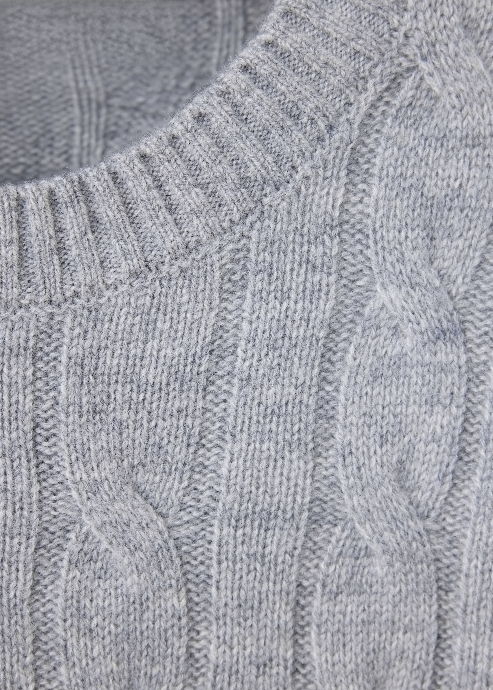 Grey cable-knit jumper close-up showing the ribbed crew neckline.