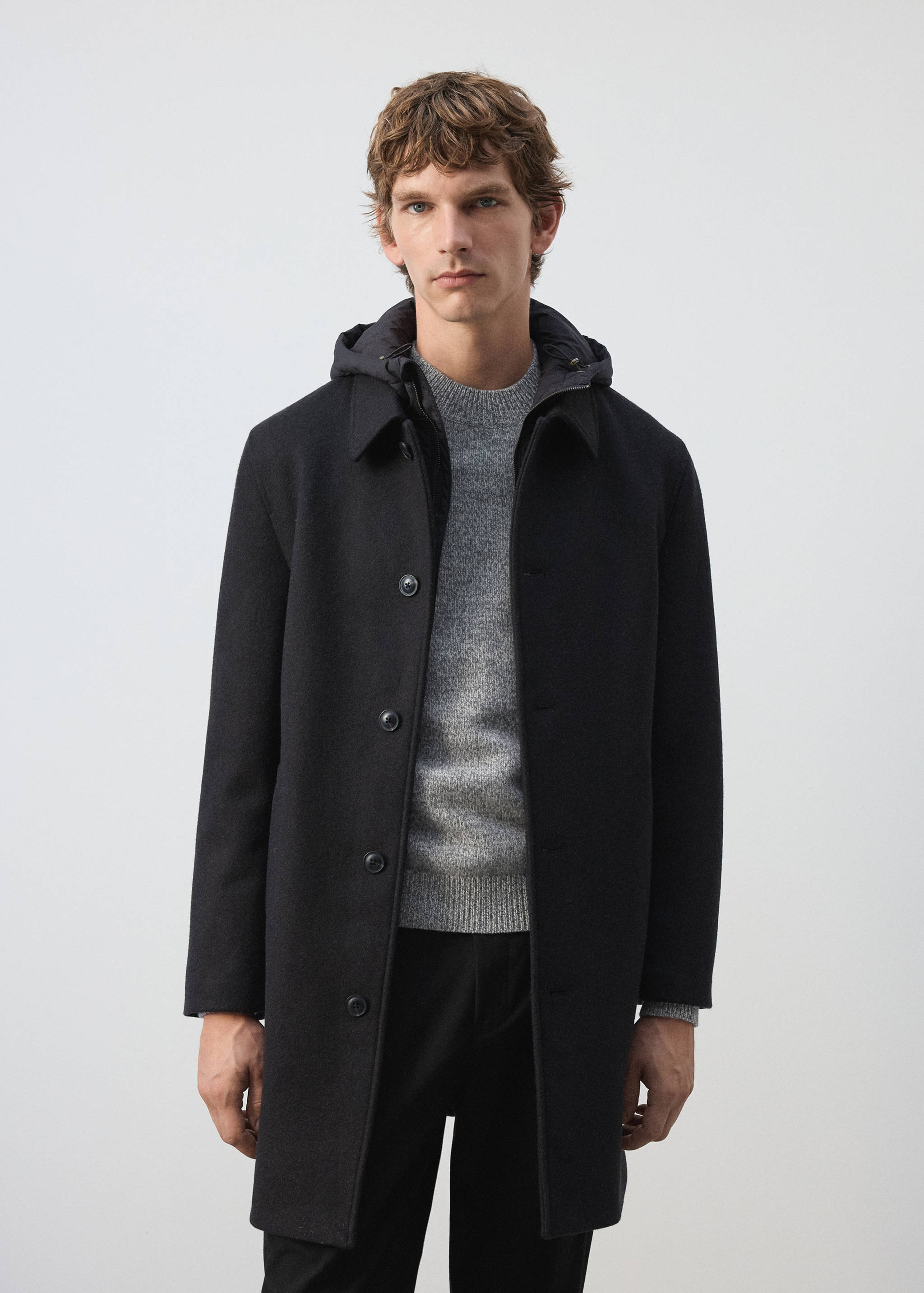 Navy blue coat with button fastening and collar, worn over a grey knit sweater.