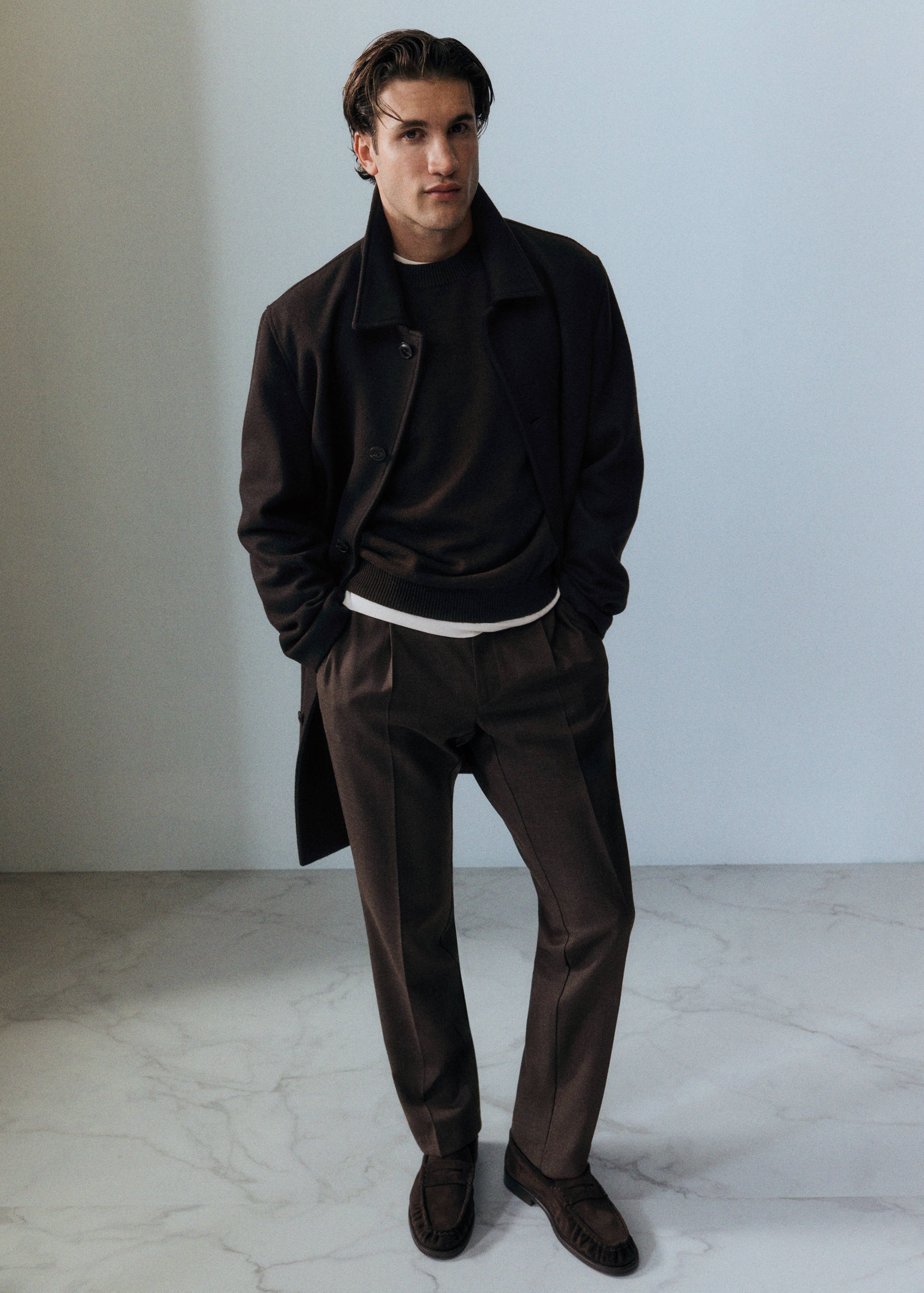 Dark brown coat with a lapel collar, worn over a dark sweater and trousers.