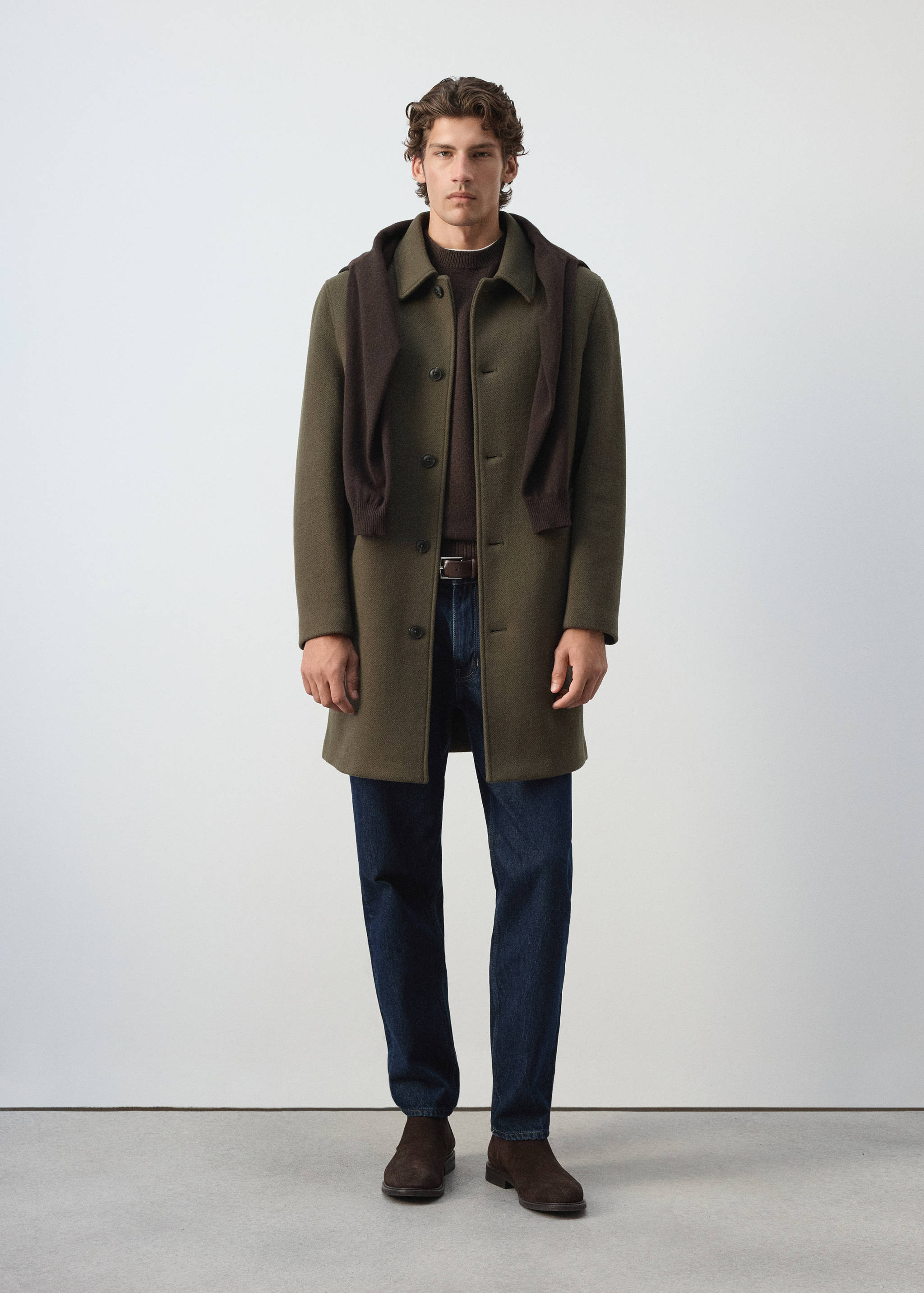 Green coat with classic collar and front button closure, styled with a brown sweater.