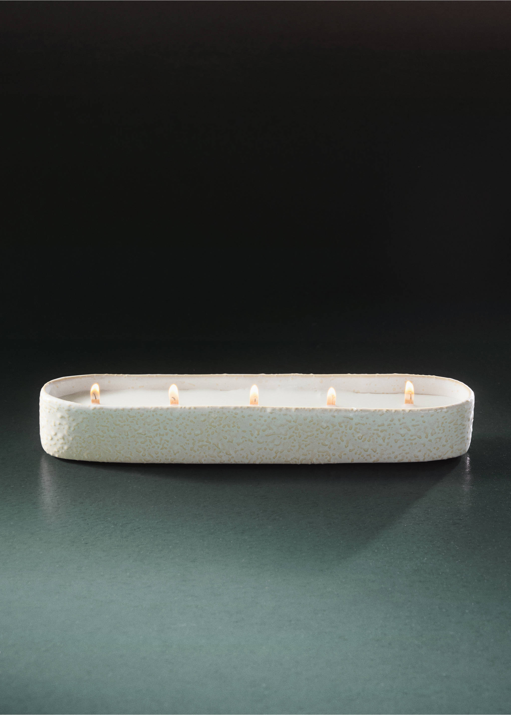 An elongated oval candle in a textured off-white container with five lit wicks., Off White. Ref: 37057904-00.