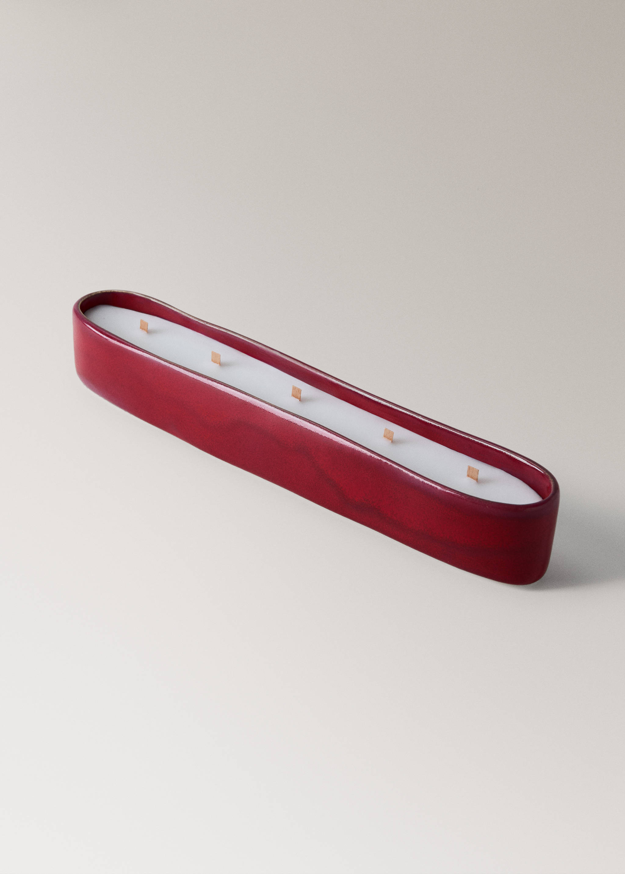 Elongated oval candle in a dark red ceramic container with five wicks.