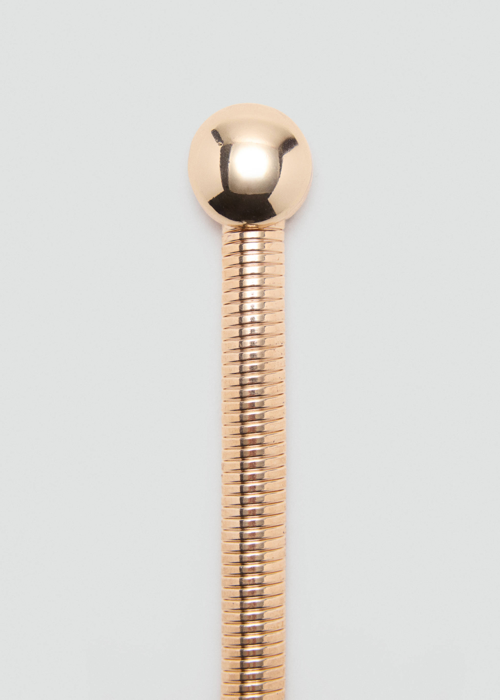 Close-up of a gold metallic belt detail featuring a snake-chain band and spherical end.