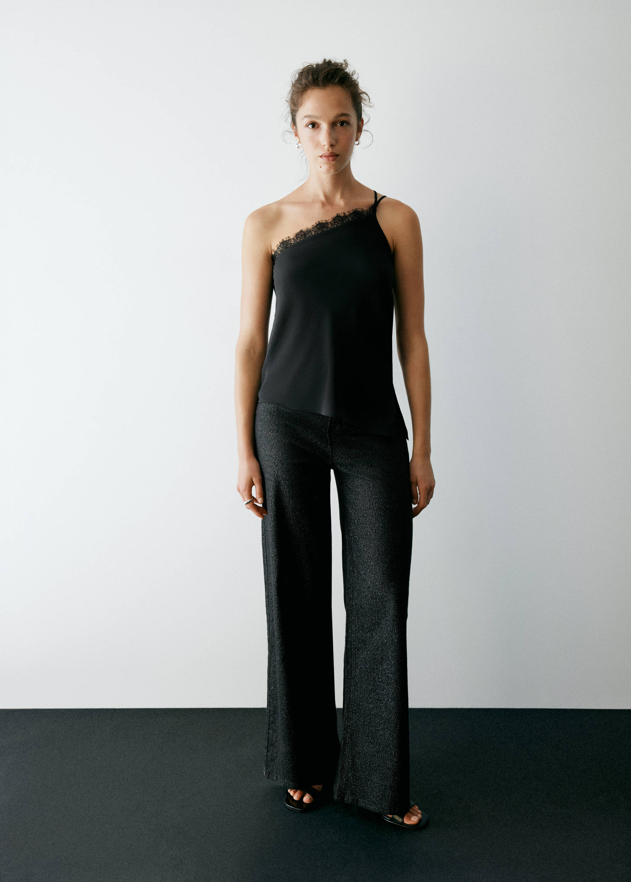 Black one-shoulder top with lace trim, worn with wide-leg trousers