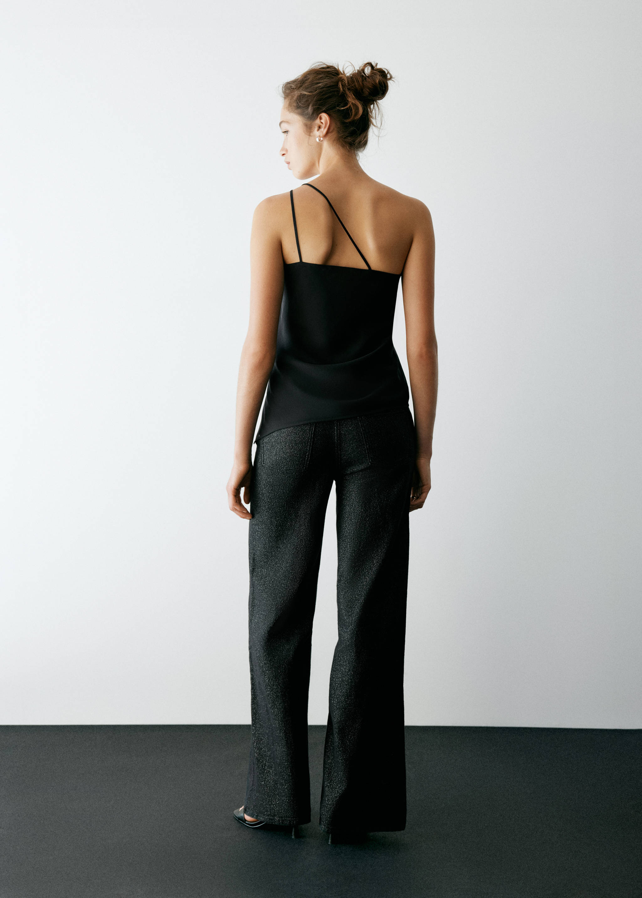 Black asymmetrical strap top from the back, paired with dark trousers.