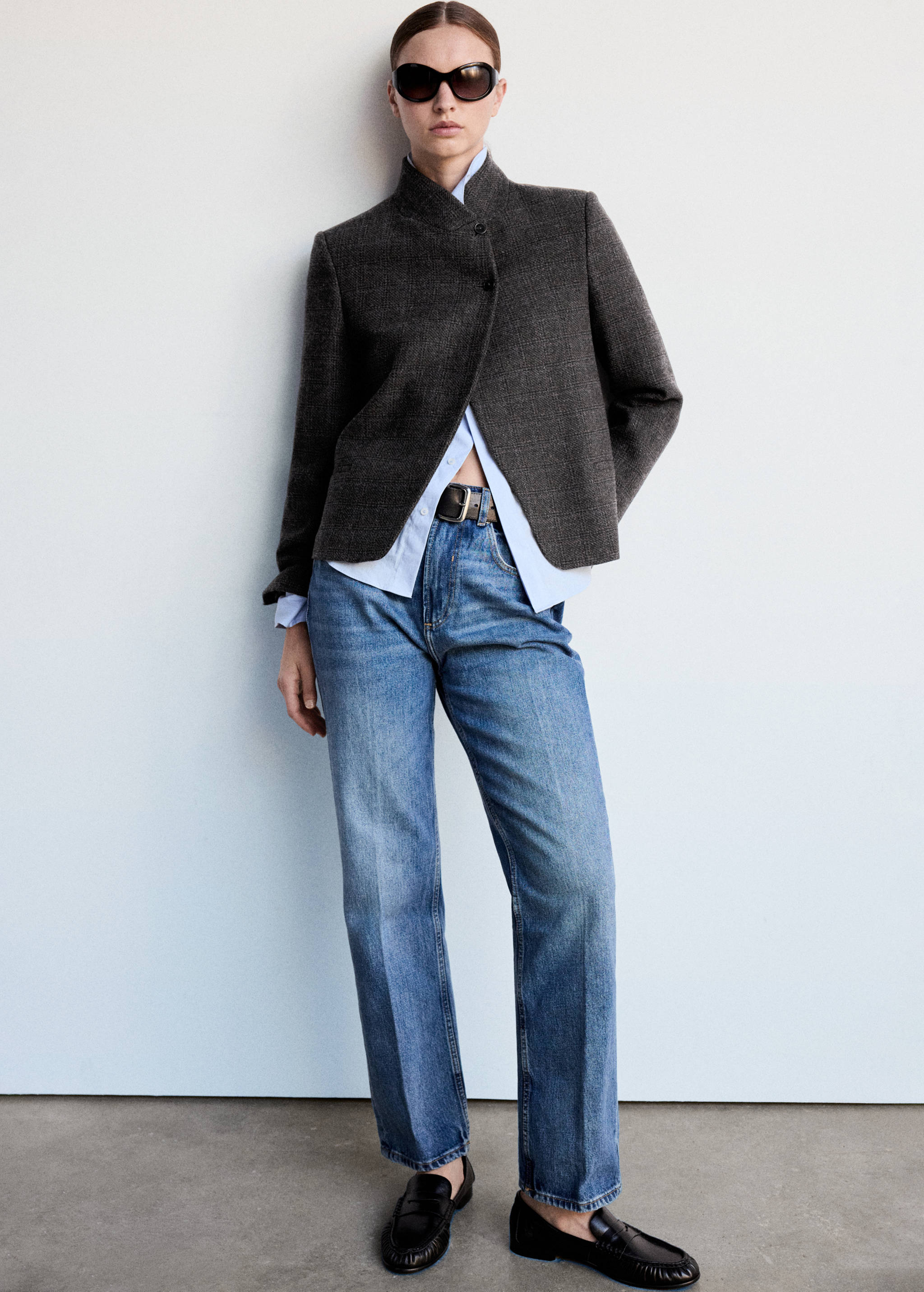 Blazer texturizado en gris antracita con cuello alto tipo cisne y cierre de botones asimétrico, combinado con vaqueros azules.