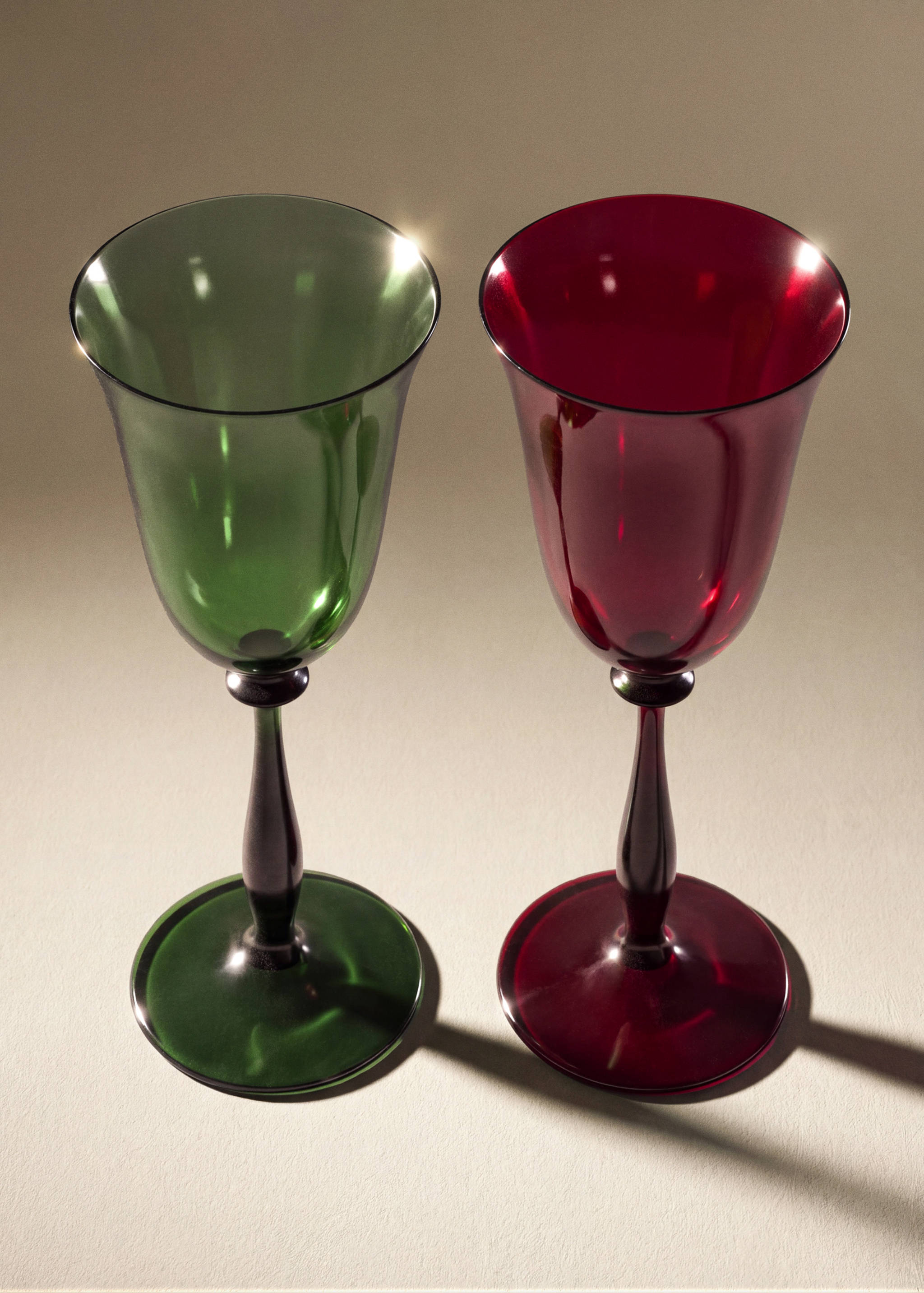 Two glass goblets in green and deep red with slender stems.