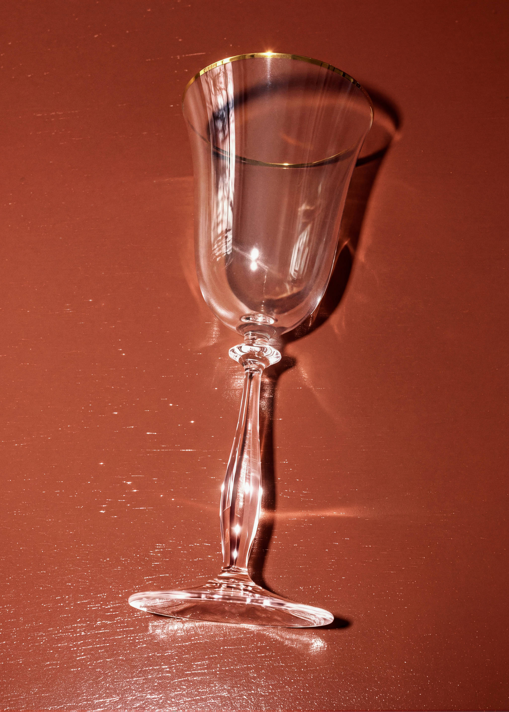 Clear glass goblet with a gold rim on a reddish-brown surface.