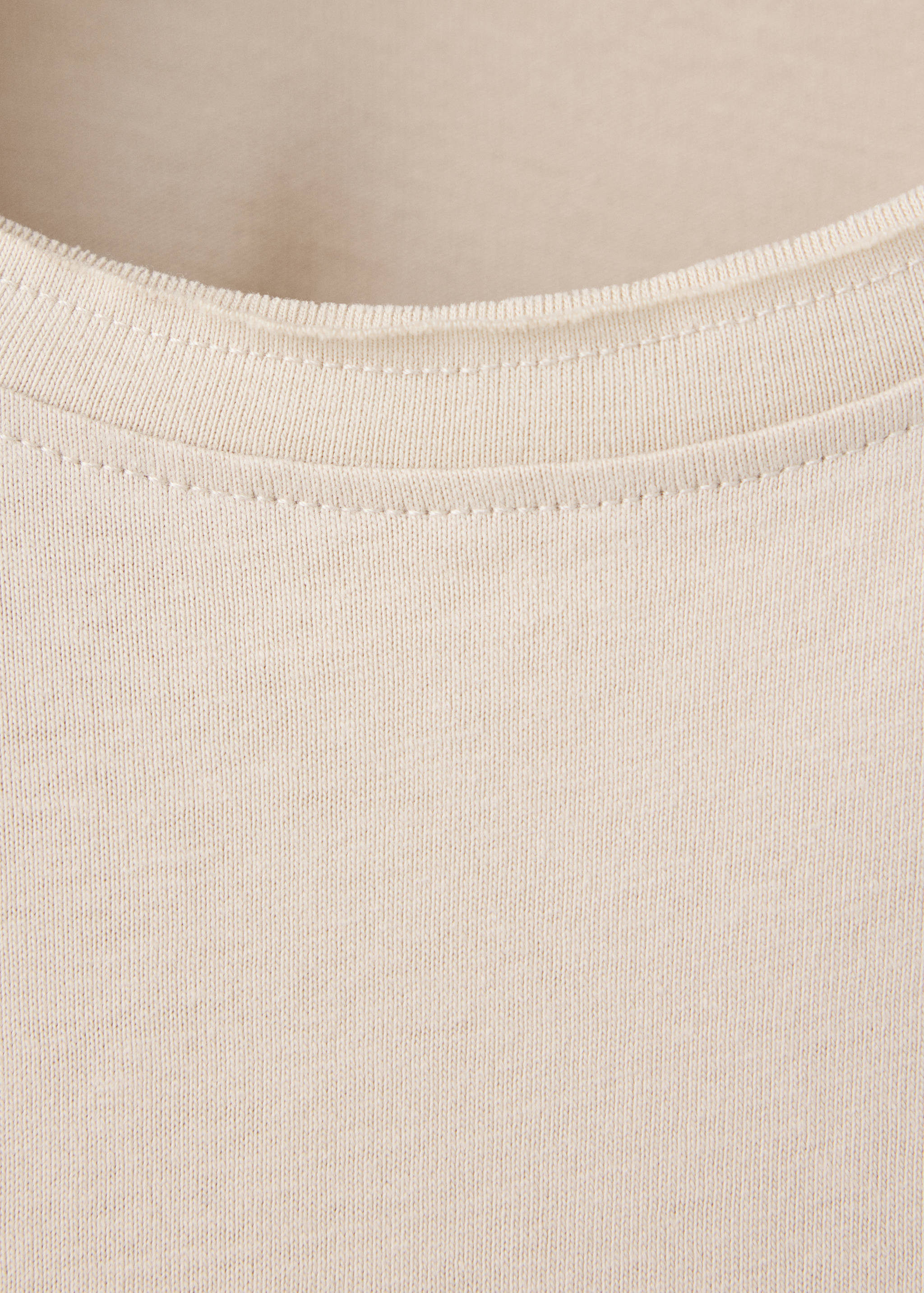 Beige t-shirt detail featuring a ribbed crew neck with raw edge.