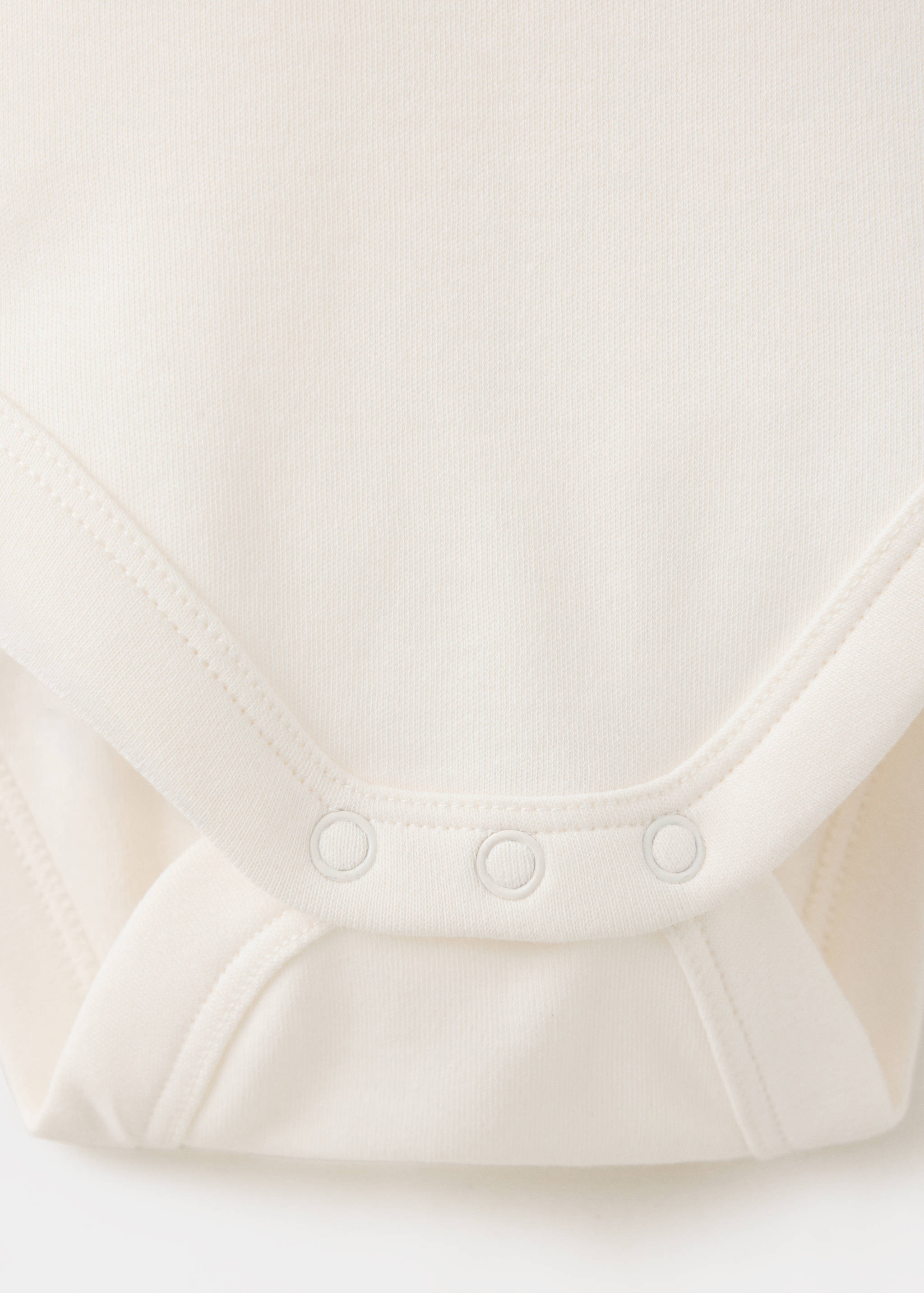 Close-up of fabric and snap button detail on an off-white baby body.