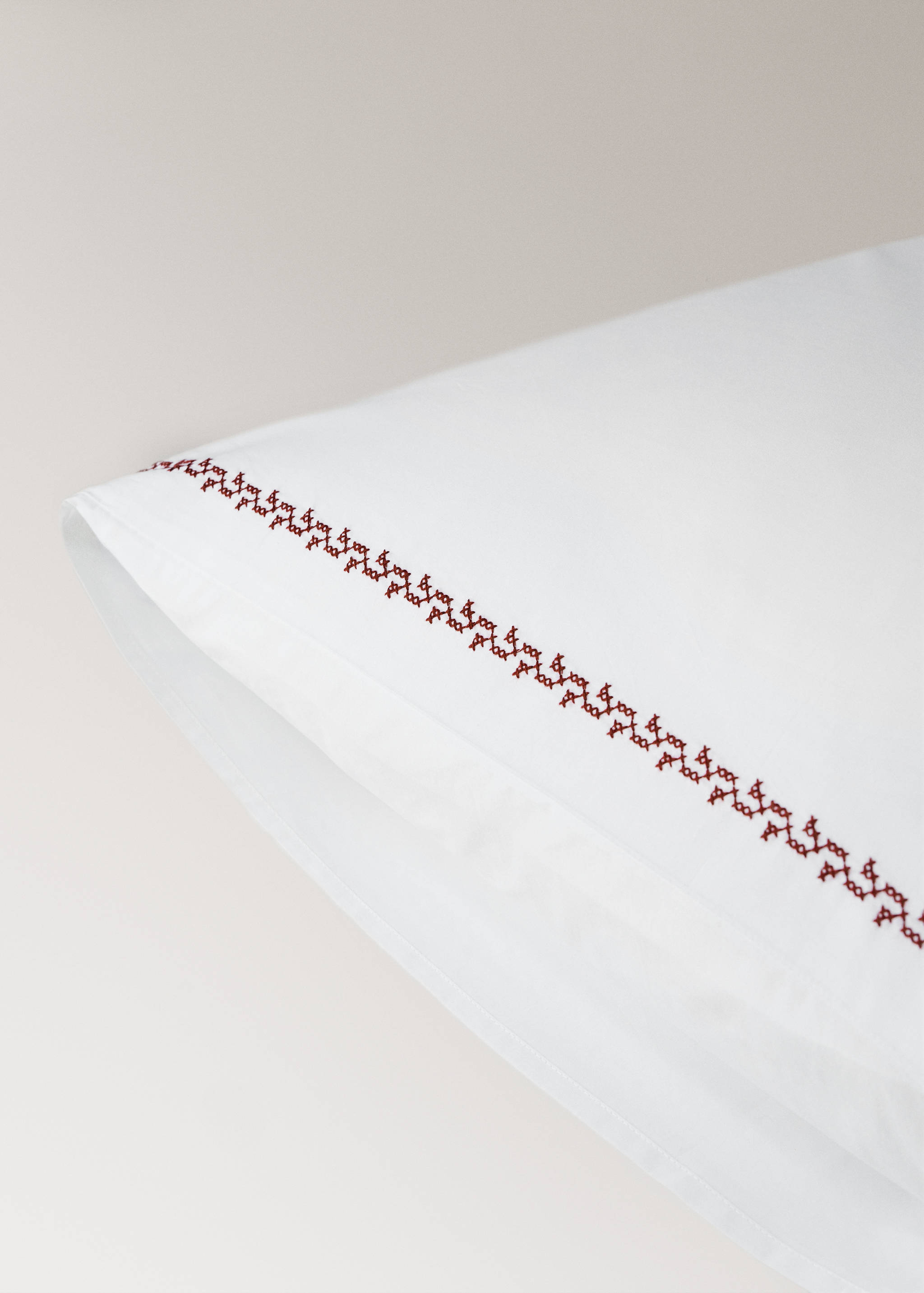 White pillowcase with a dark red embroidered border detail.