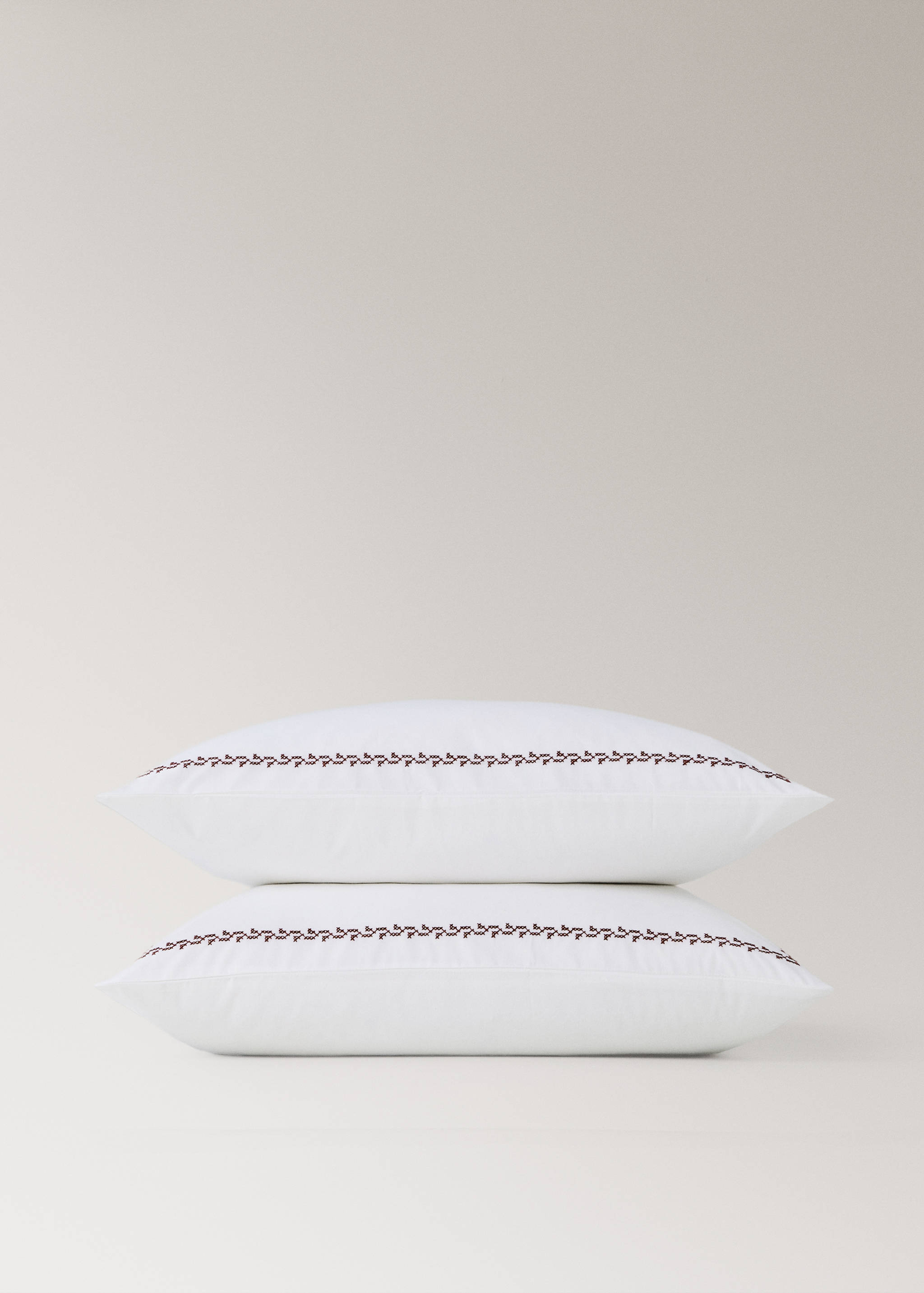 Two stacked white pillowcases featuring a dark brown embroidered border.