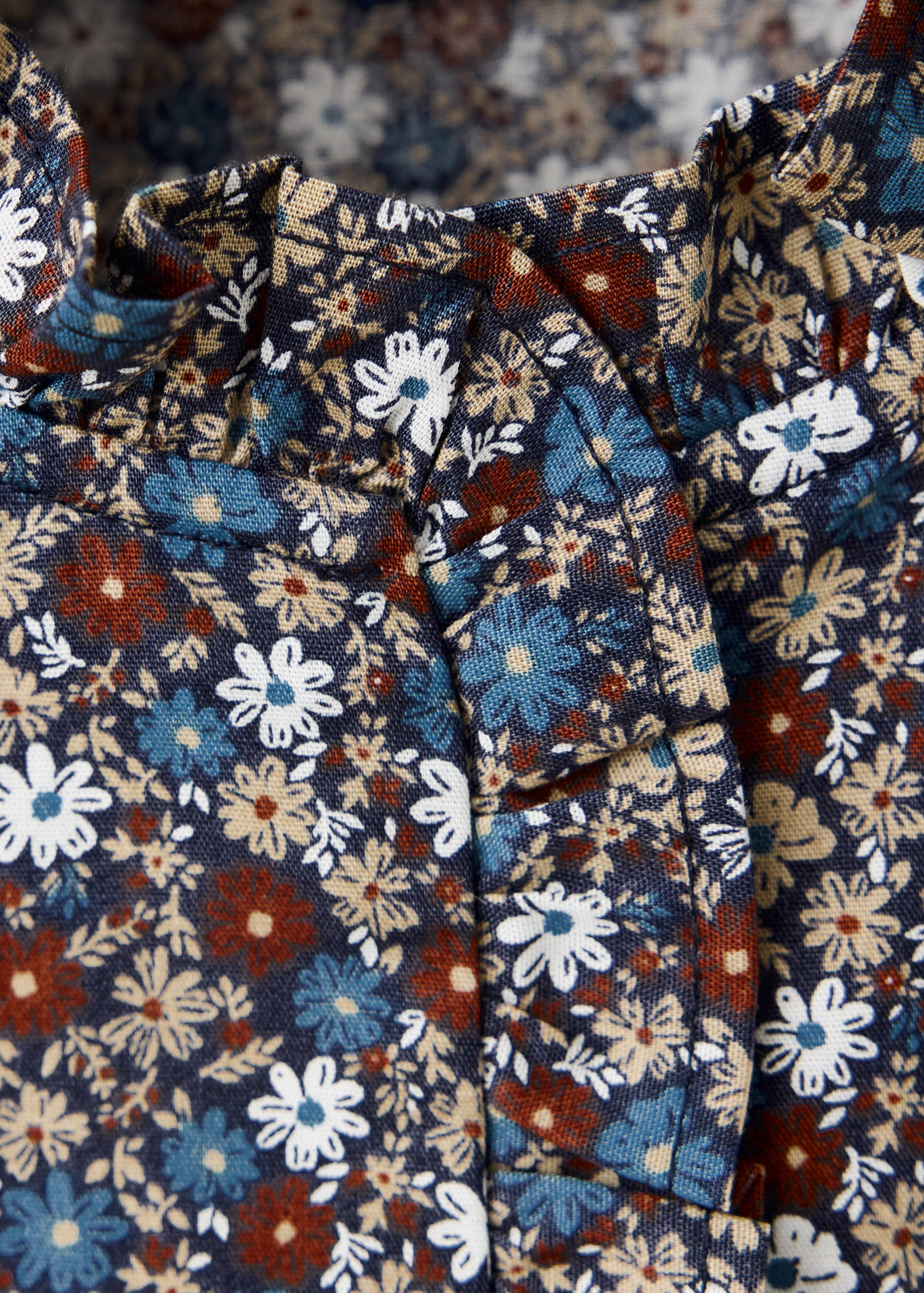 Close-up of a dark blue floral print shirt featuring a ruffled high neck.