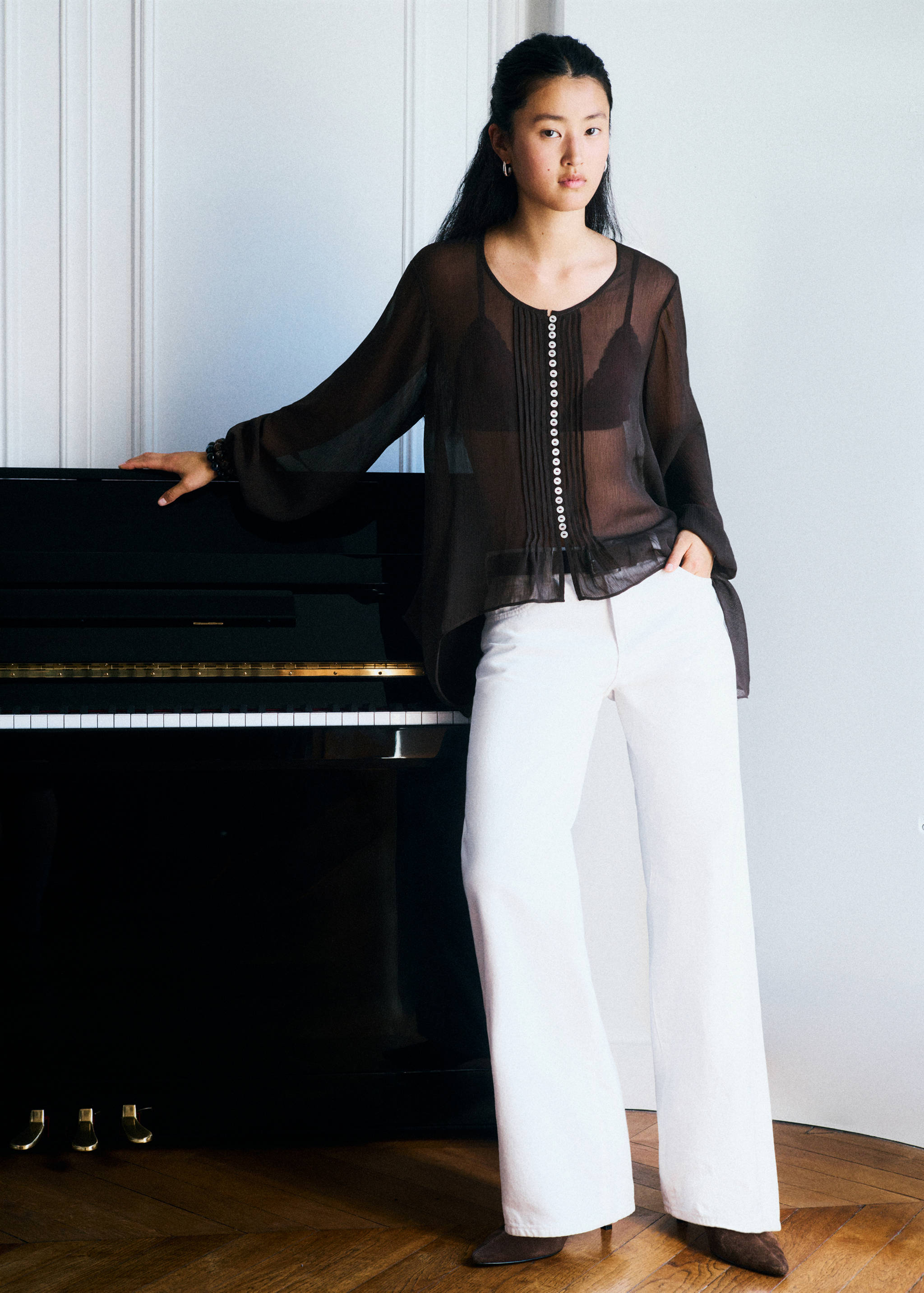 Sheer dark brown blouse with a buttoned front, worn with white trousers.