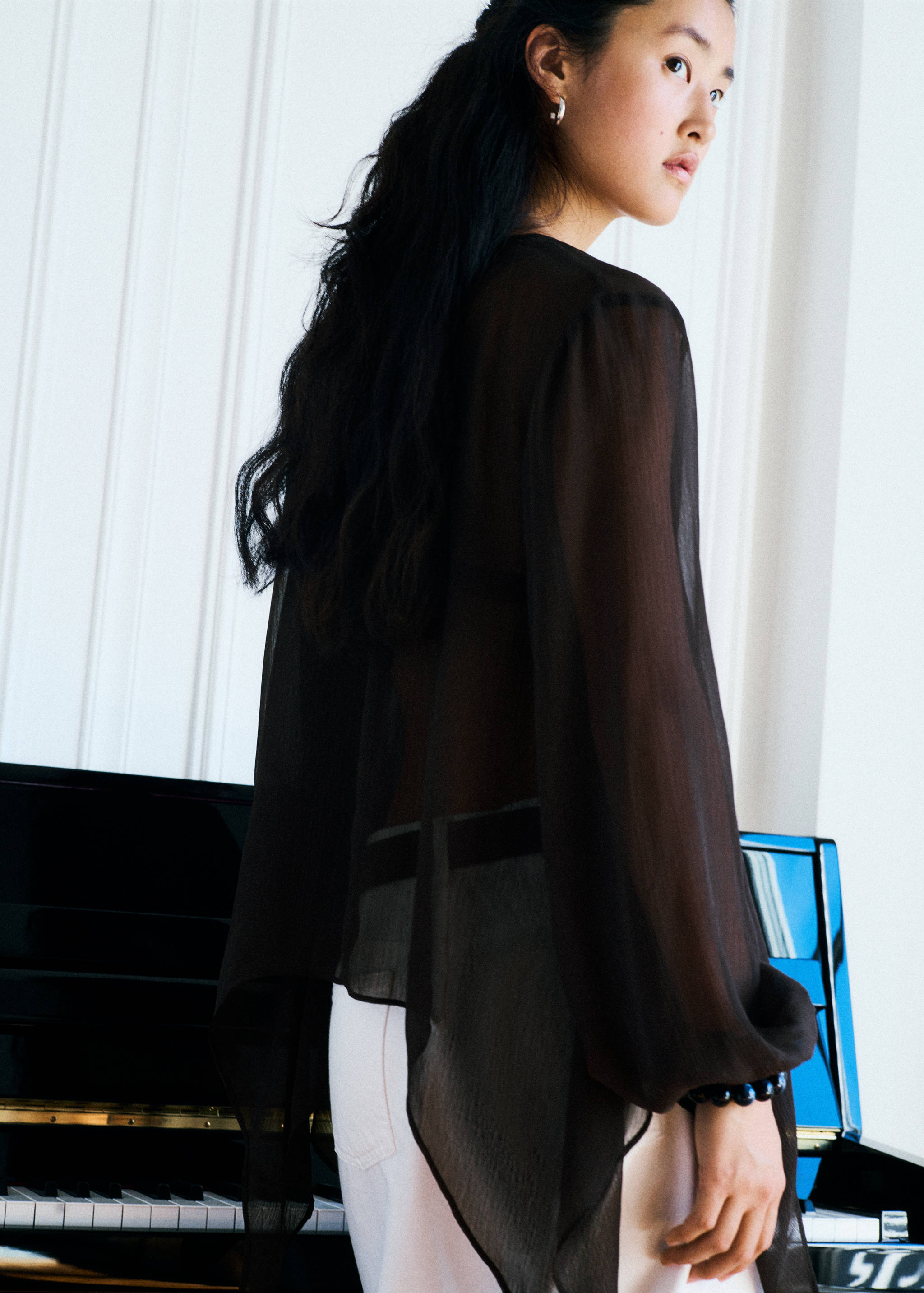 Black sheer blouse with long sleeves and asymmetrical hem, back view.