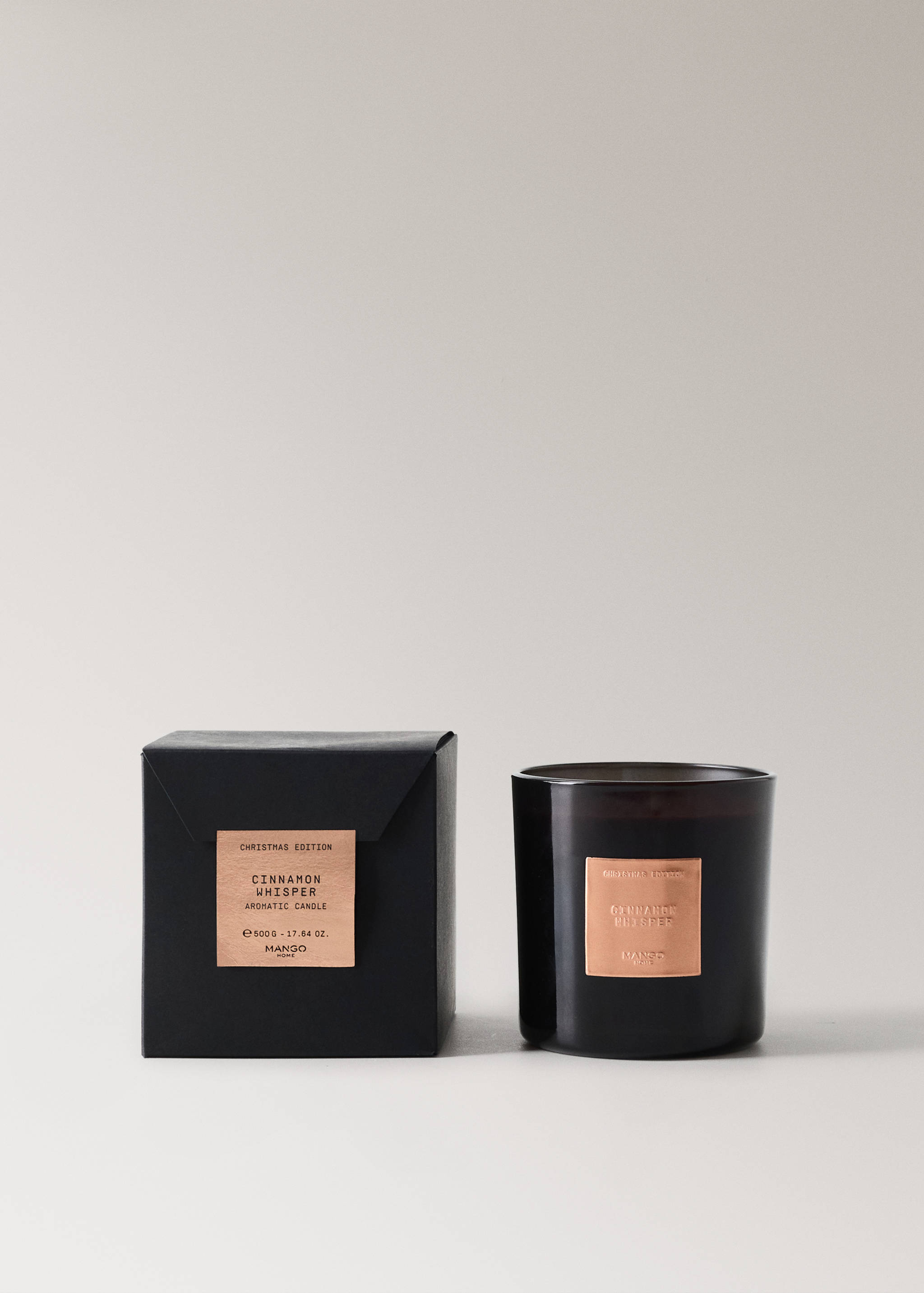 A dark scented candle in a glass jar with a copper label, shown with its black presentation box.