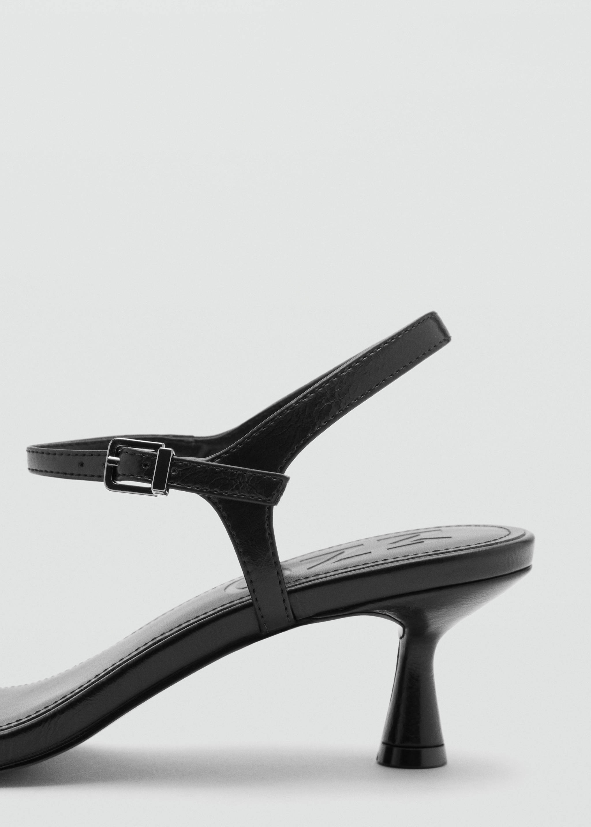 Close-up of the heel and buckled strap detail on a black sandal.