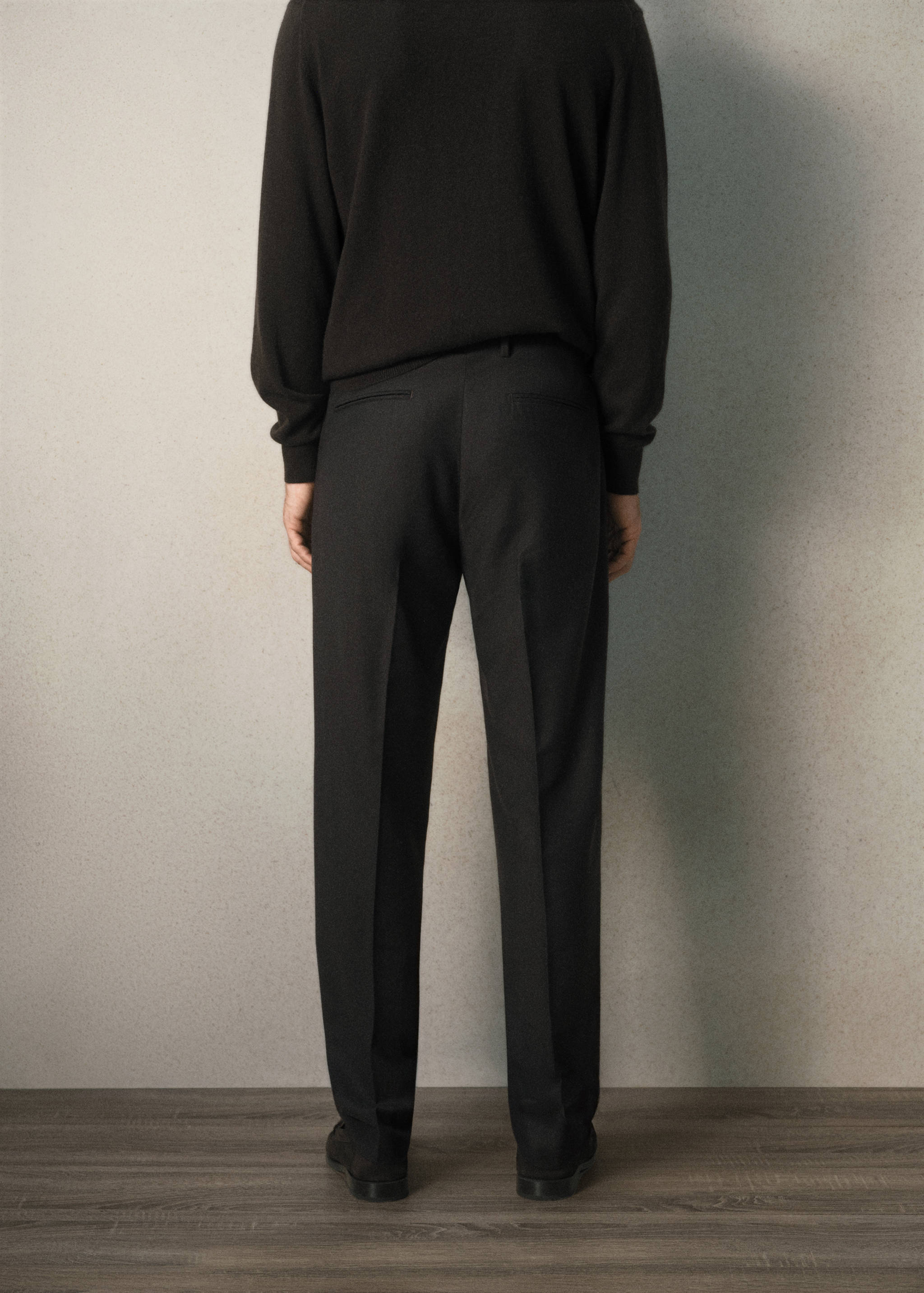 Back view of dark trousers with pressed creases worn with a black sweater.