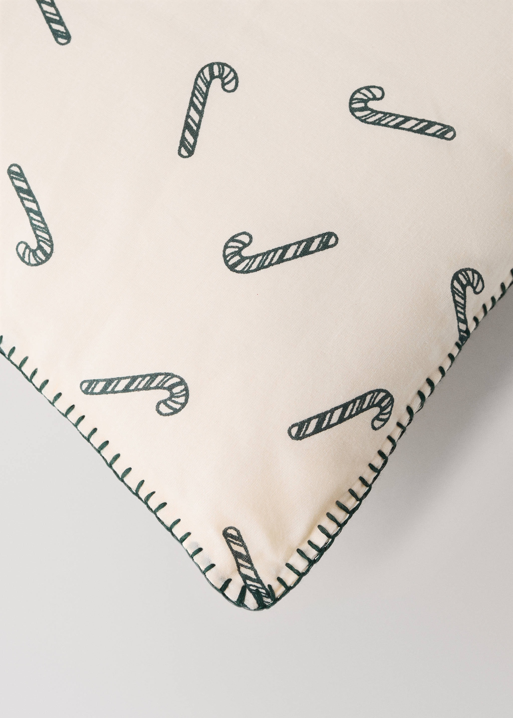 Cream cushion with a dark green candy cane print and whipstitch trim.