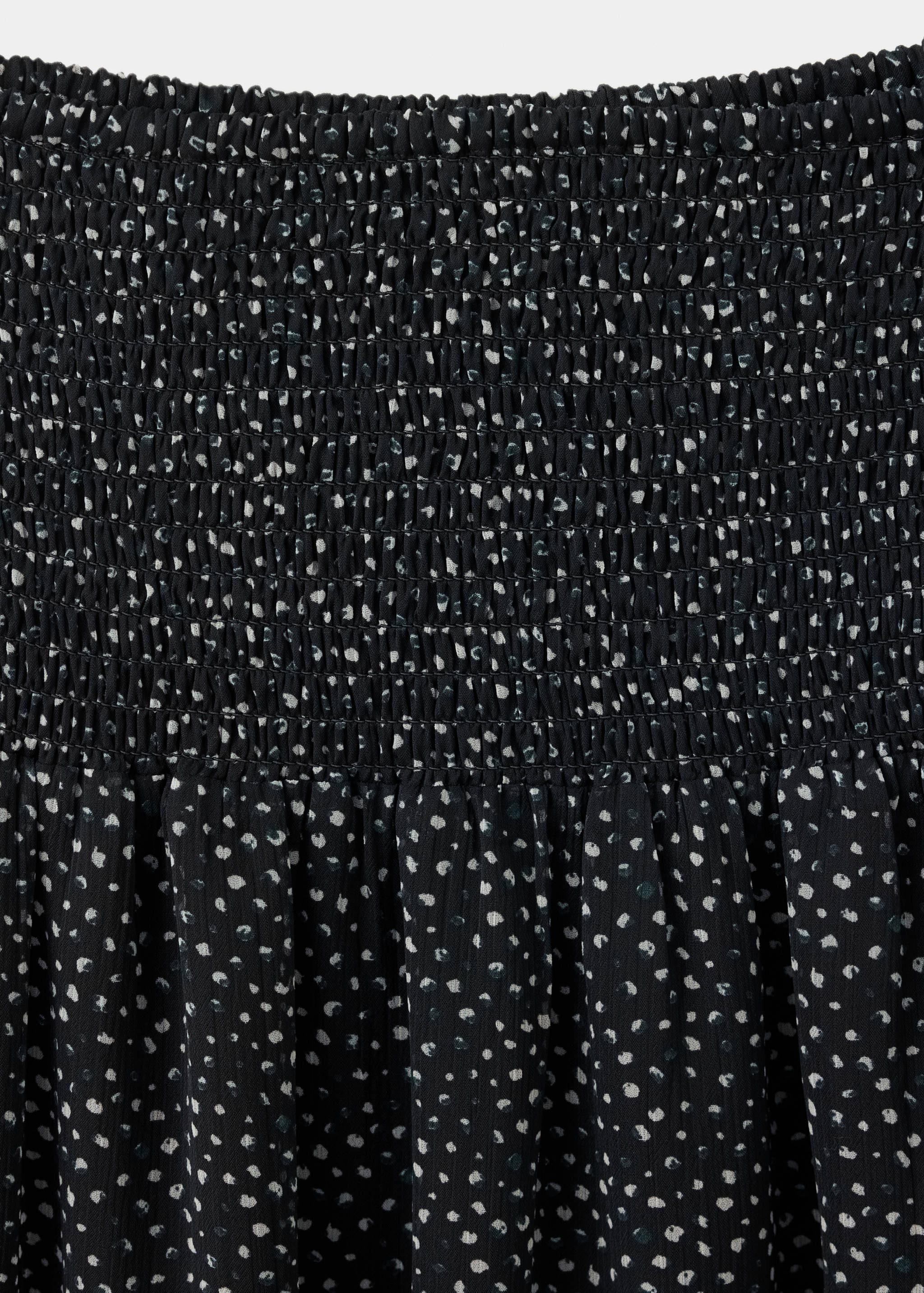 Detalle de falda negra con cintura elástica fruncida y estampado de lunares blancos y verde azulado.