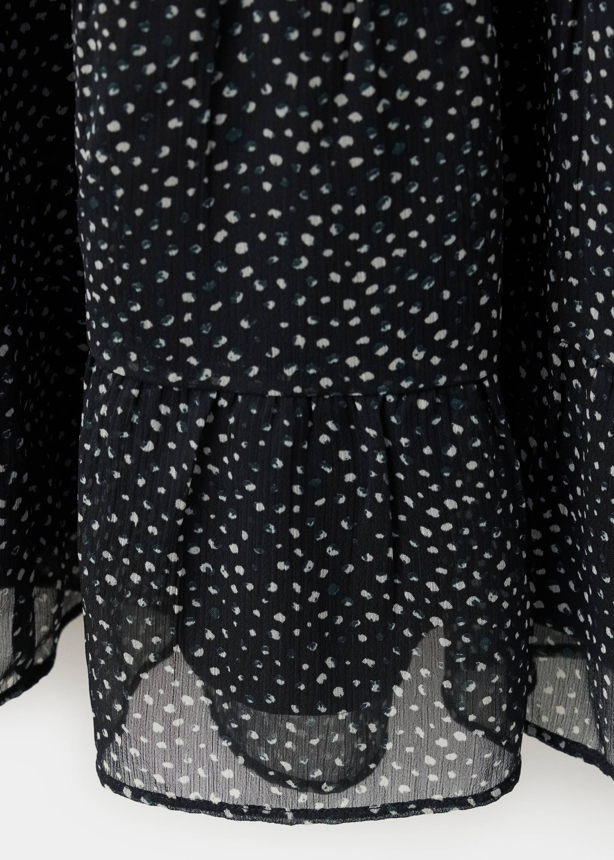 Detalle de tejido de una falda oscura estampada con motivos de lunares y bajo con volante.