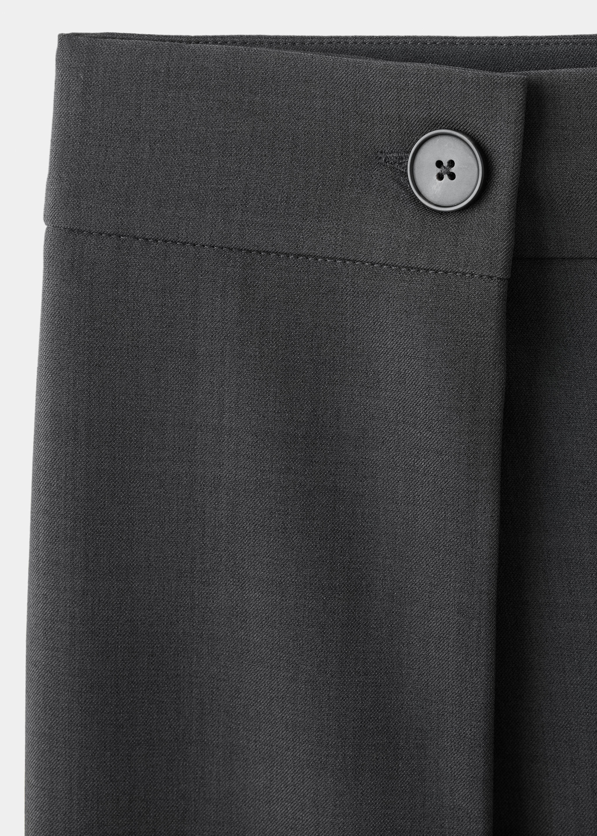 Close-up of dark grey trousers waistband and button detail.