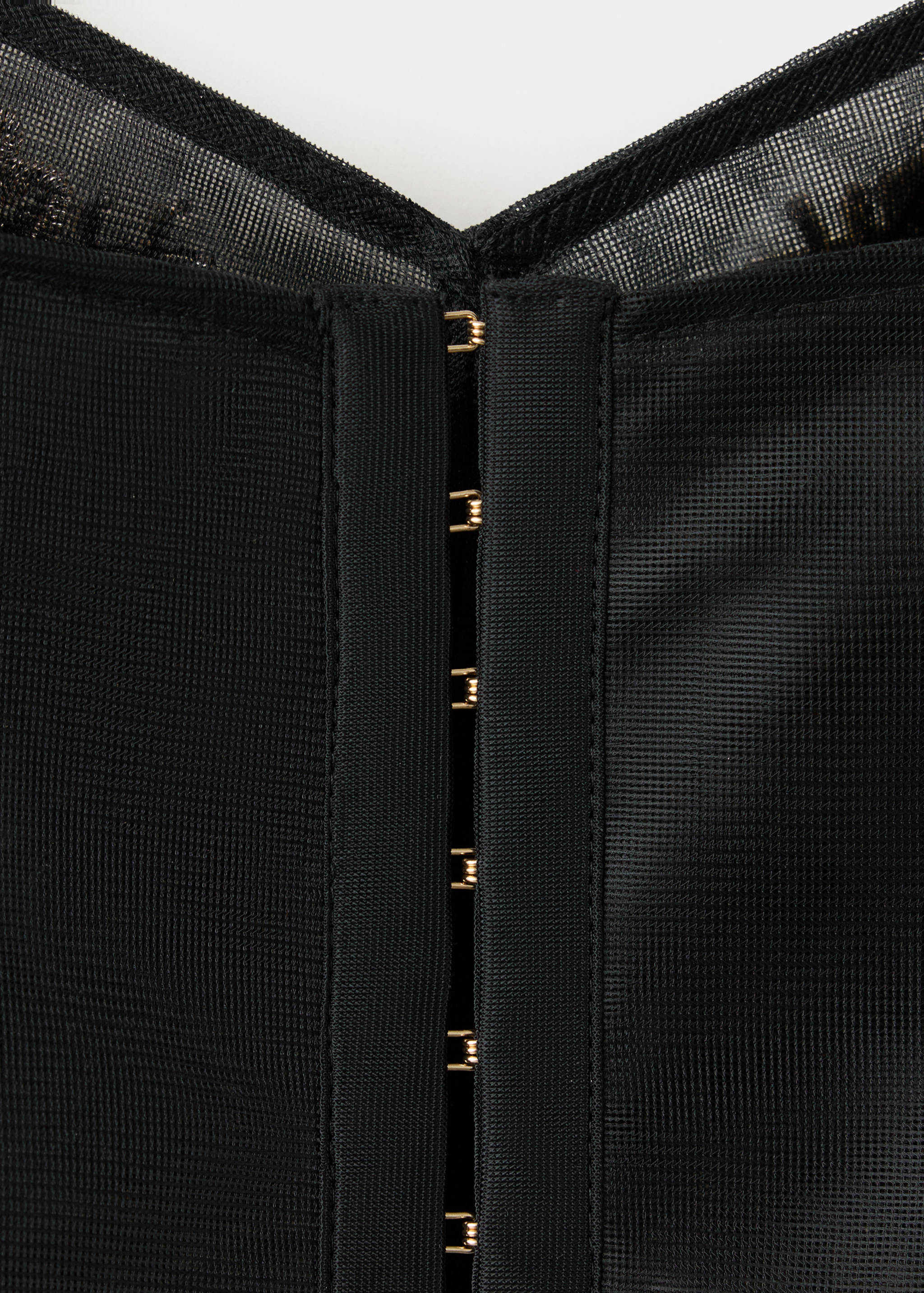 Close-up of a black mesh top with gold-toned hook-and-eye fastenings.