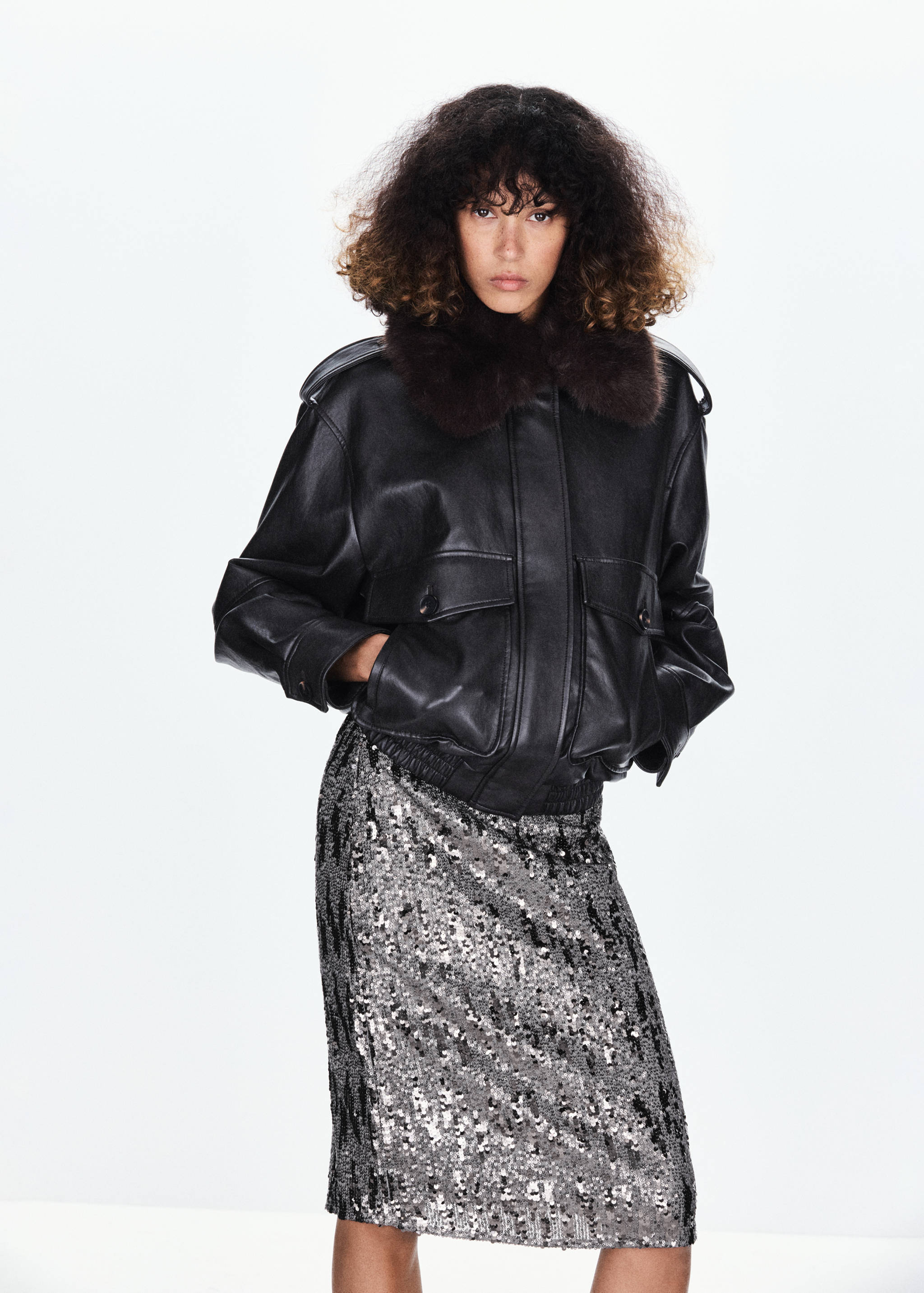 Silver sequinned knee-length skirt worn with a black jacket featuring a faux-fur collar.