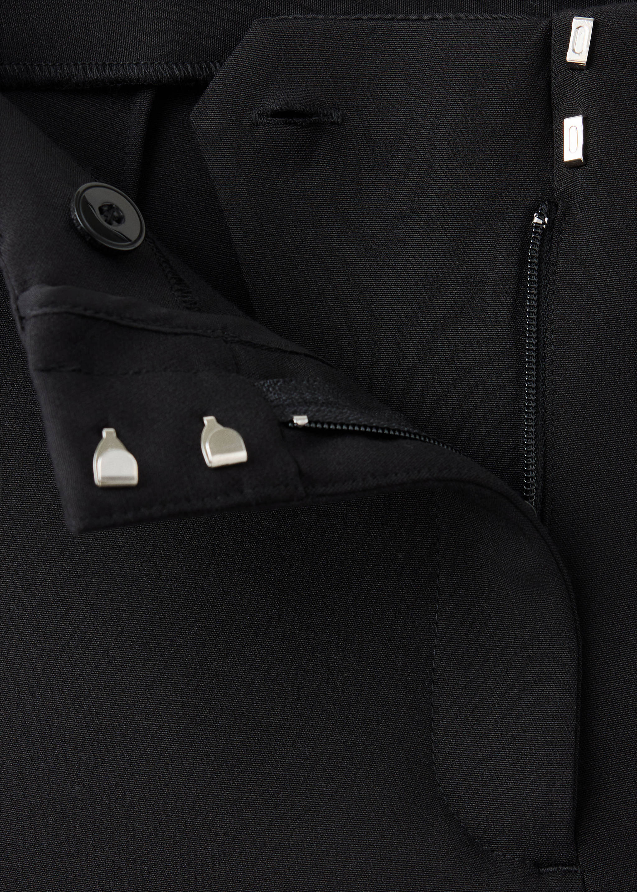 Close-up of black trousers waistband with hook-and-eye and button fastening.