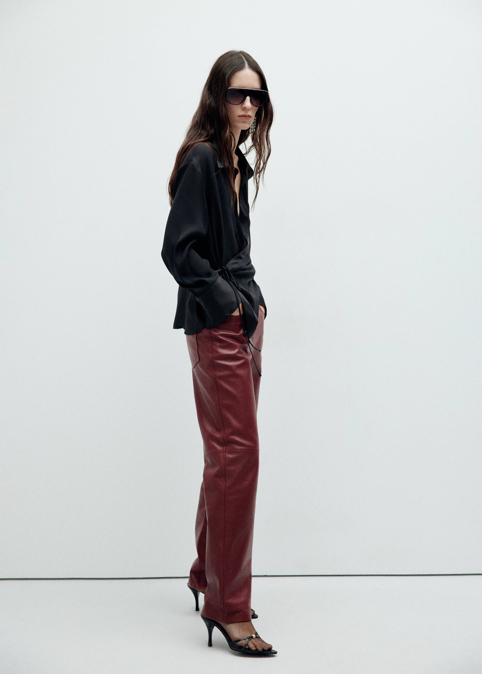 Black wrap shirt with long sleeves and side ties, worn with burgundy trousers.