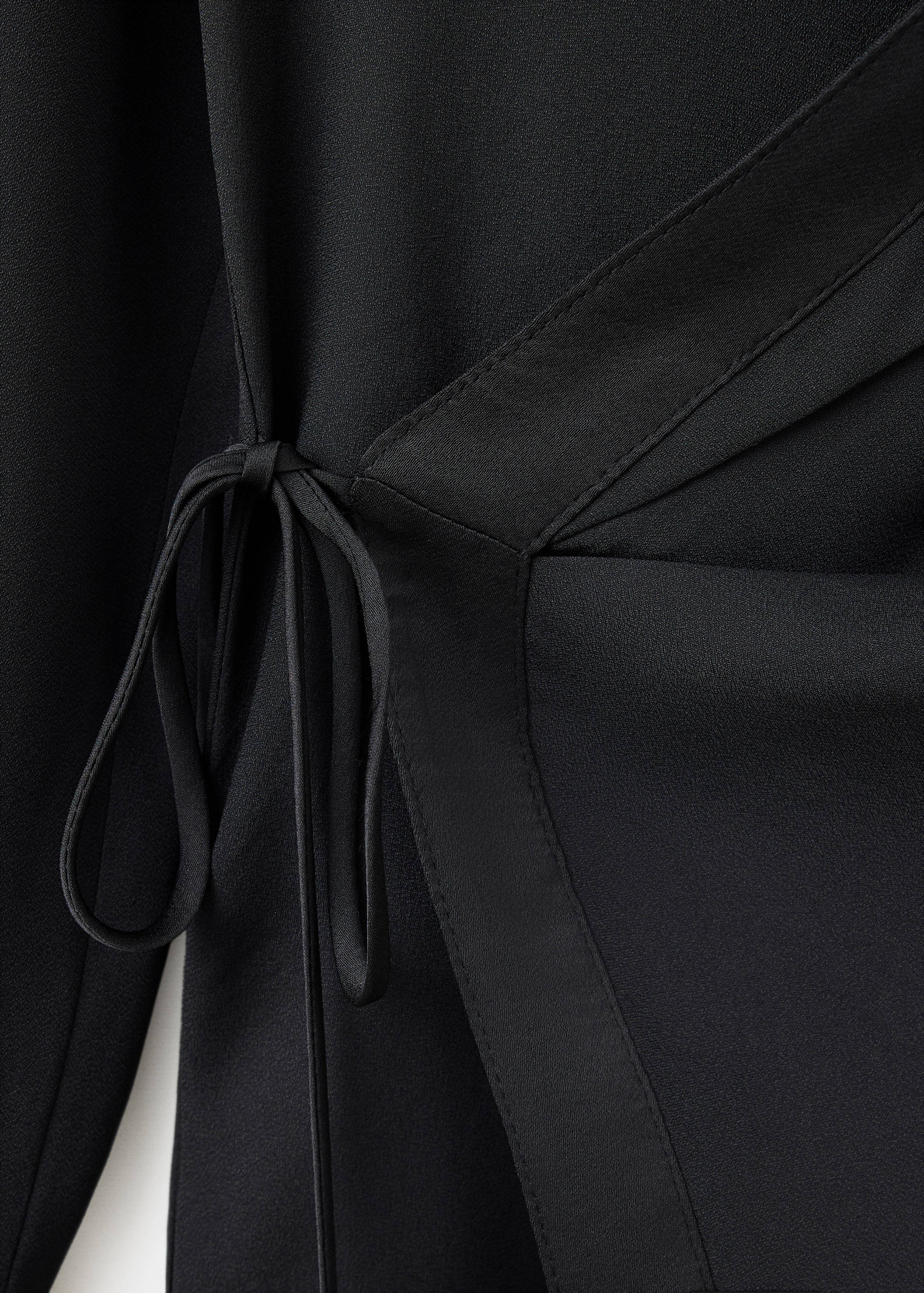 Close-up of a black shirt featuring a wrap design with side tie fastenings.