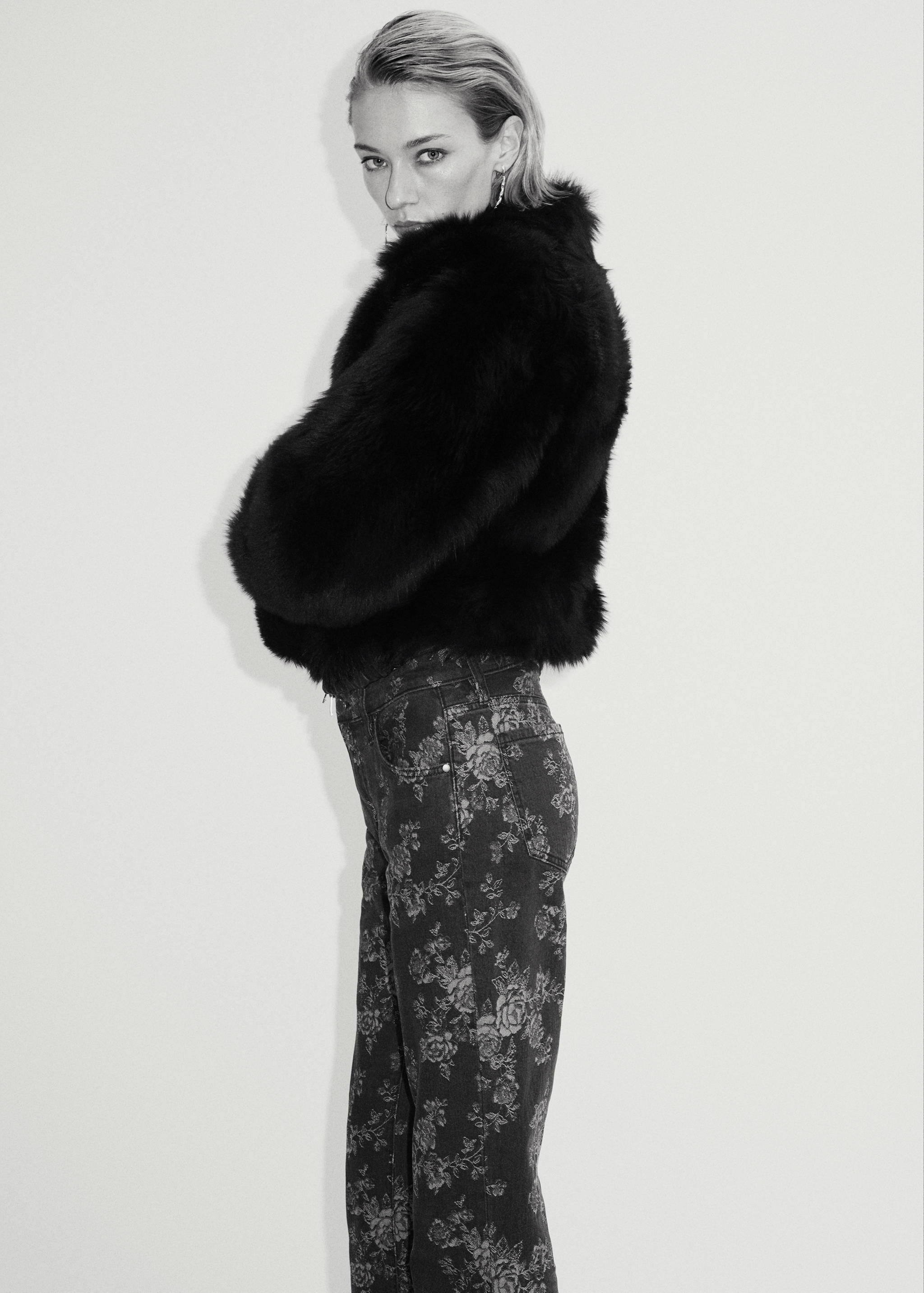 Dark grey floral print denim trousers worn with a black faux-fur jacket.