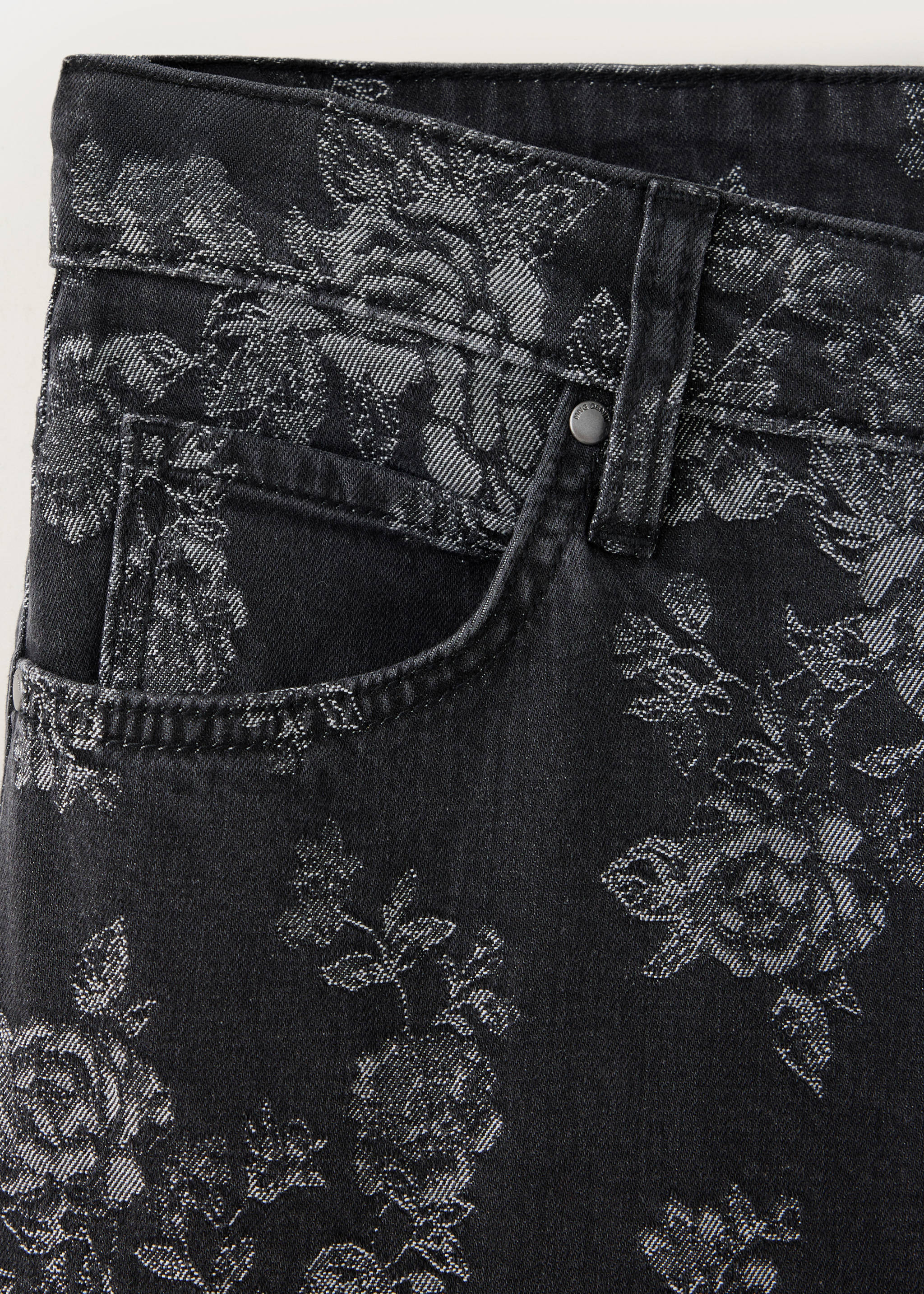 Close-up of black denim trousers featuring a silvery floral pattern.