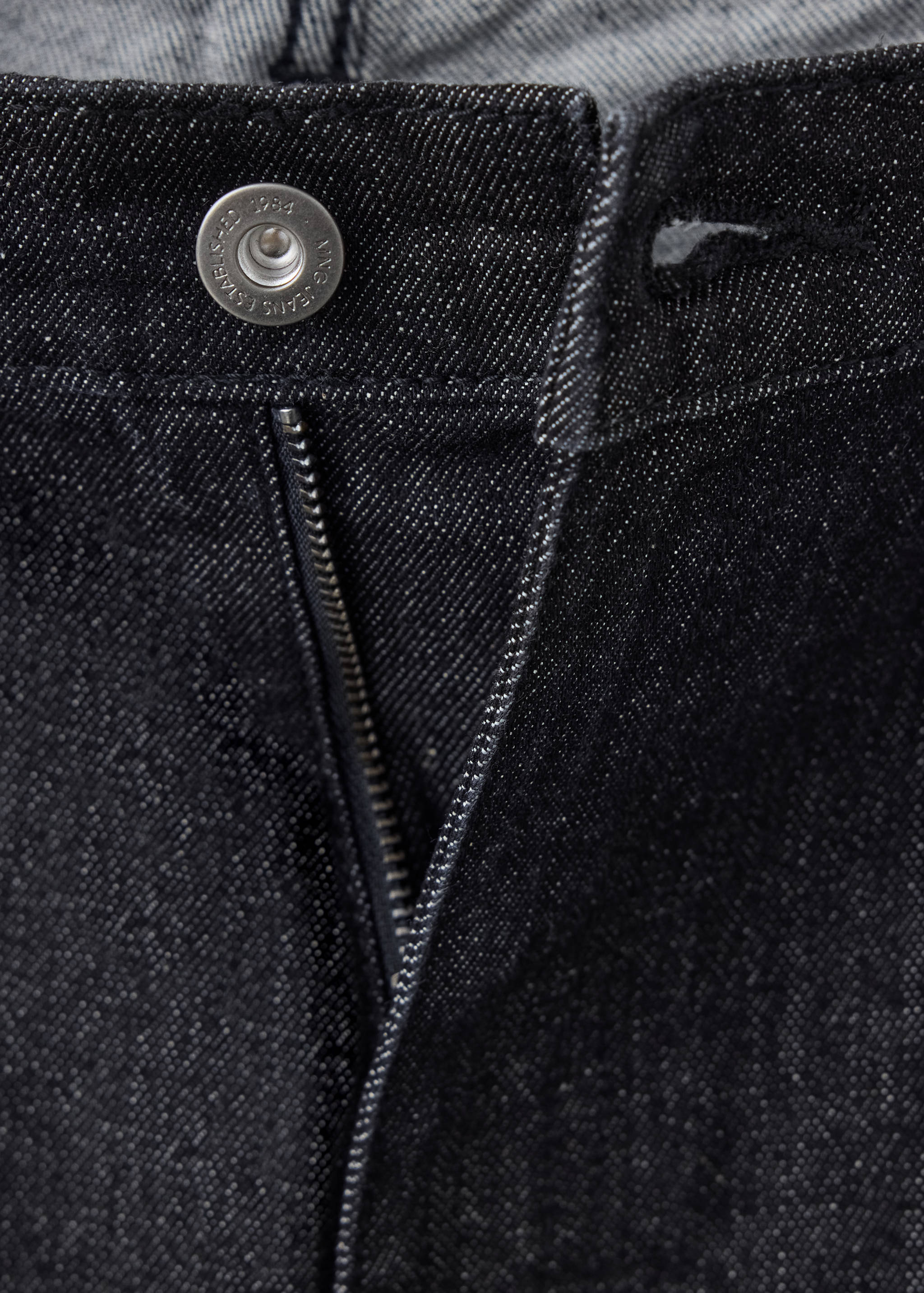 Primer plano de la cinturilla y la bragueta con cremallera en unos pantalones vaqueros oscuros.