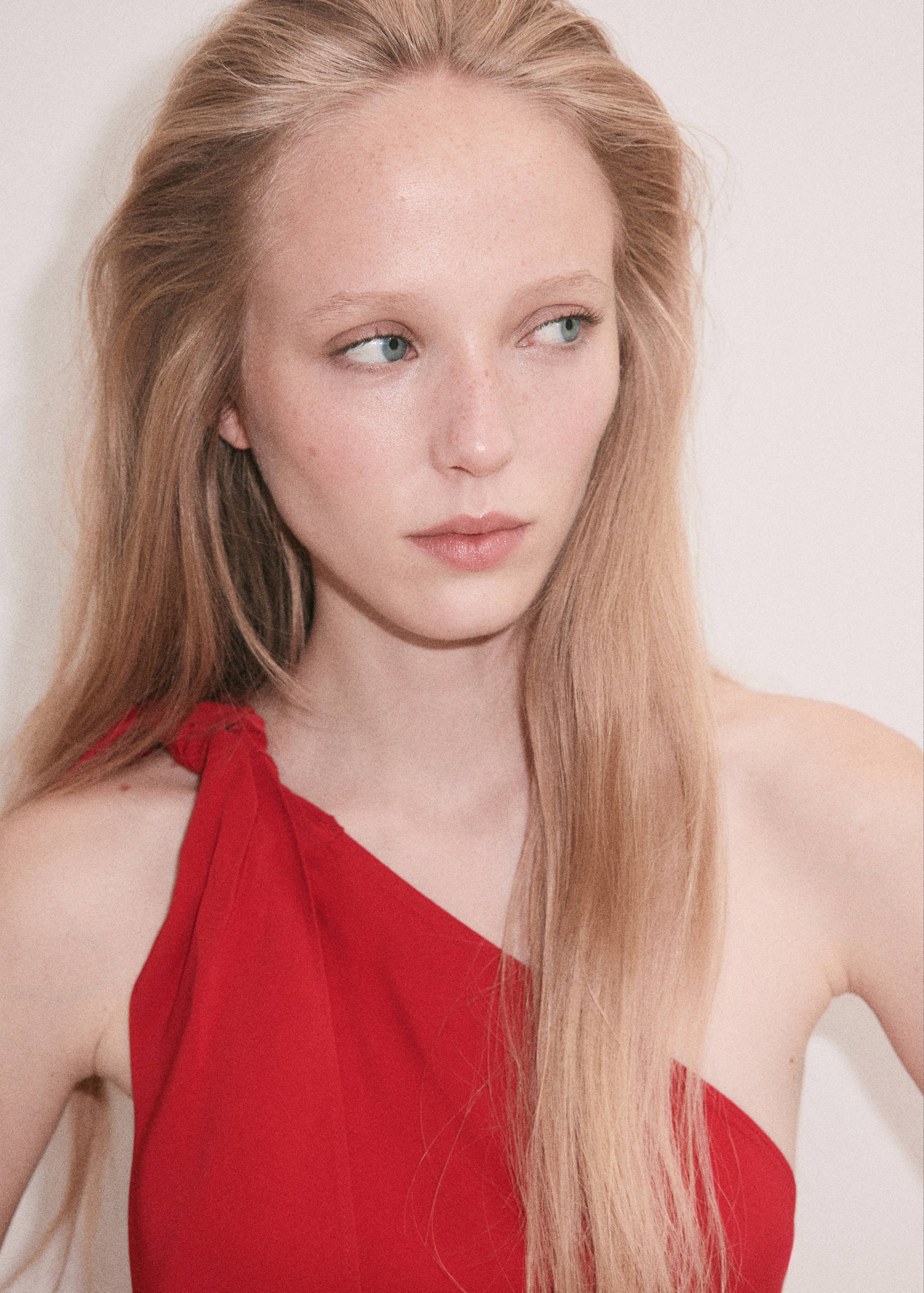 Close-up of a model wearing a red one-shoulder dress with a knotted strap detail.