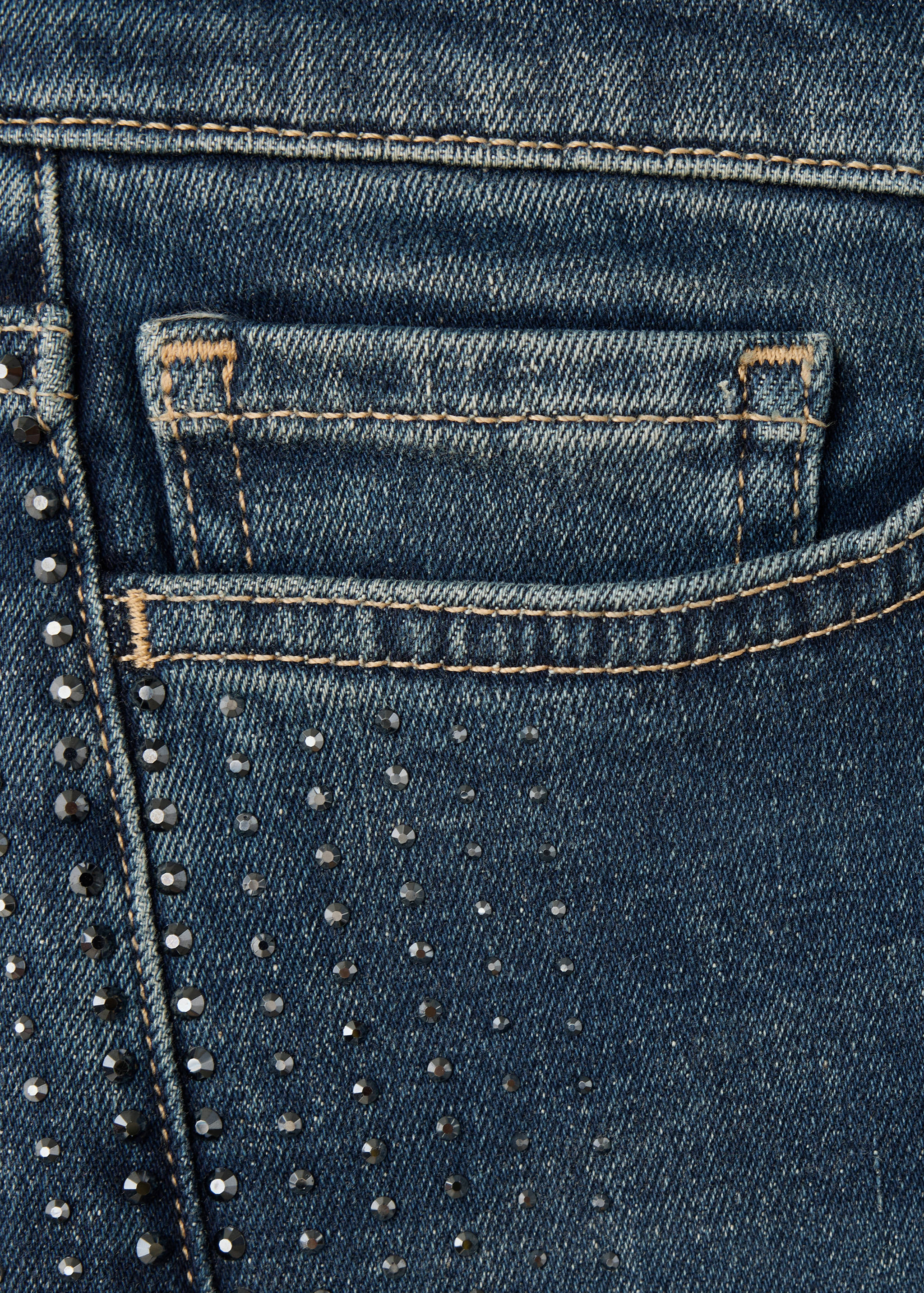 Close-up of blue denim trousers with rhinestones and contrast stitching.