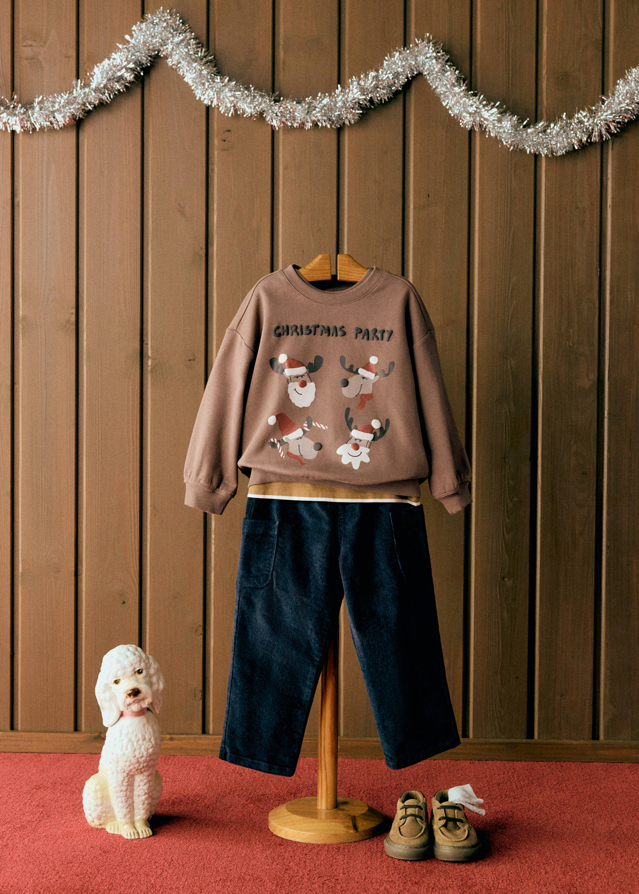 Brown Christmas party sweatshirt with reindeer graphic, styled with navy trousers.