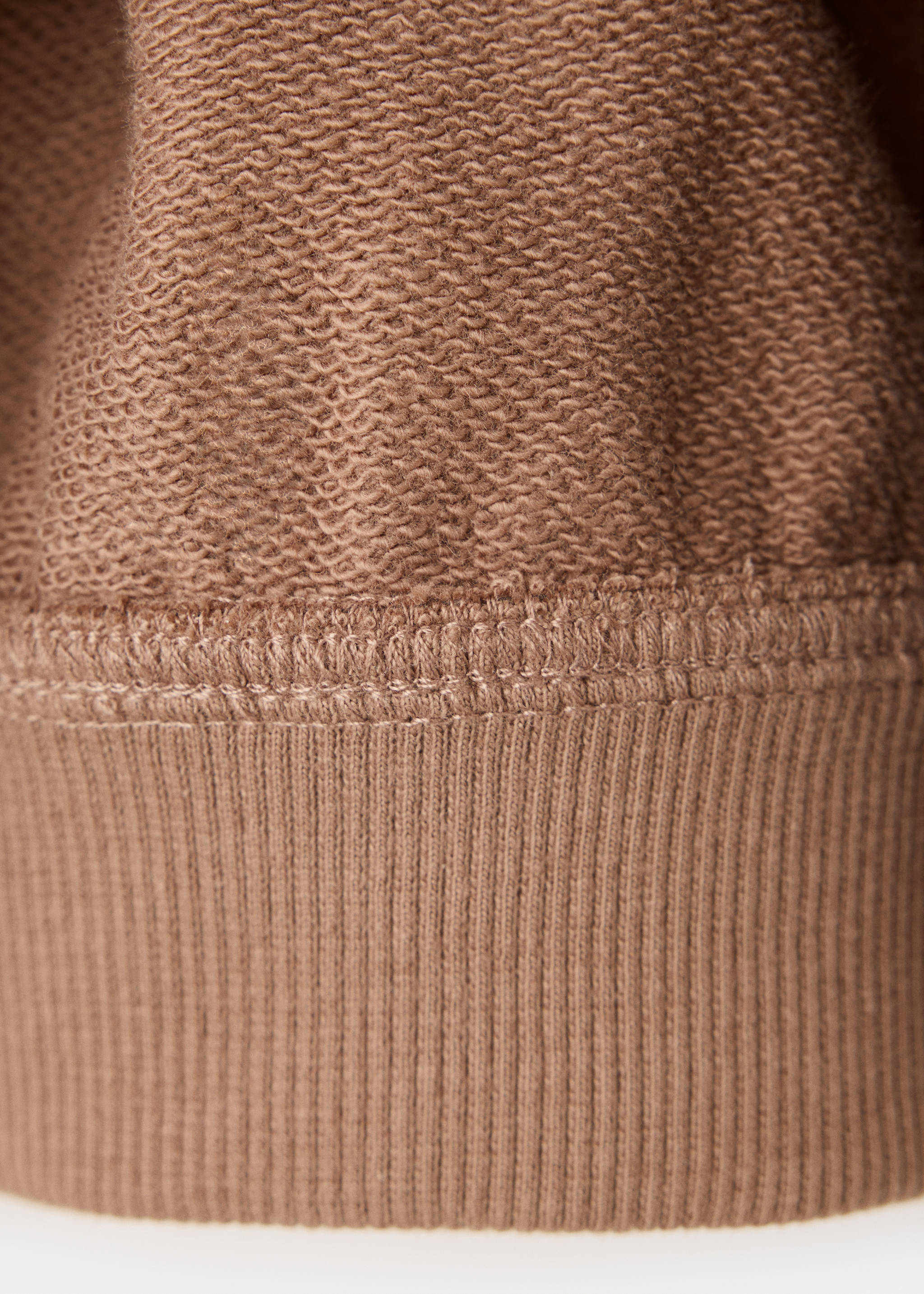 Detalle de la textura del tejido y el bajo de canalé de la sudadera marrón.